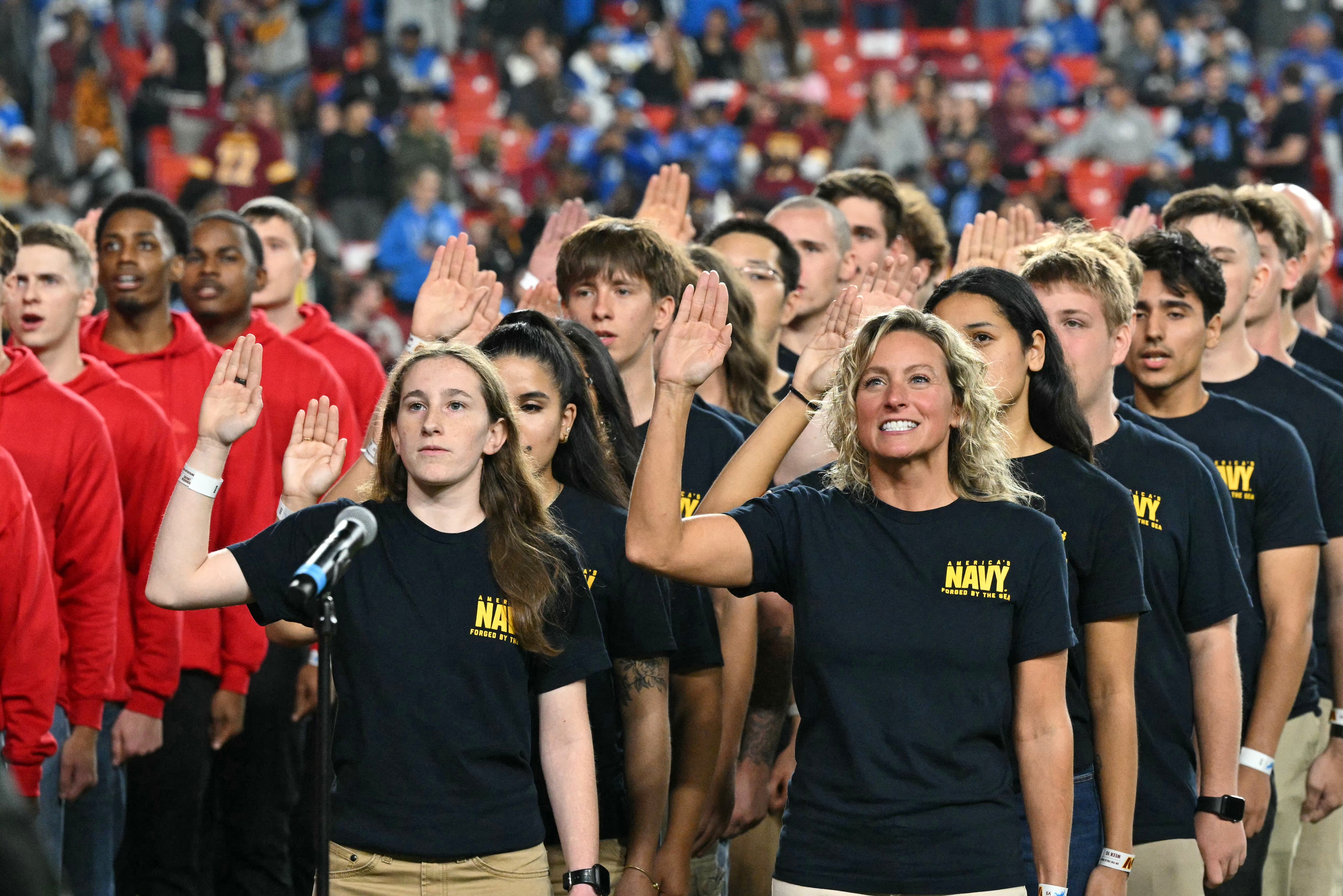 Service members raise their hands as they take the oath during a reenlisting ceremony presided over by Trump during the NFL game between the Washington Commanders and the Detroit Lions at Northwest Stadium in Landover, Maryland