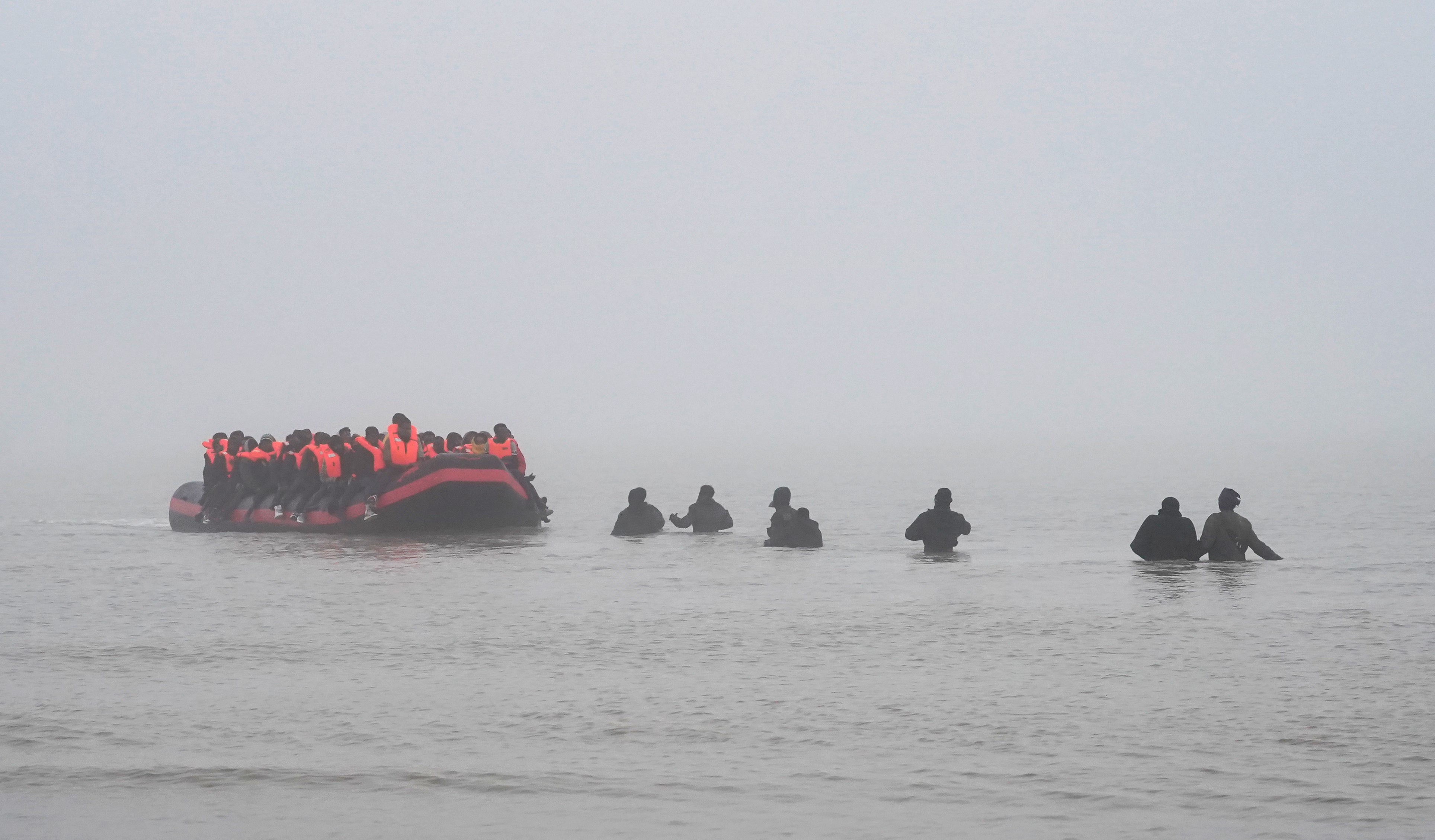 People wade through shallow water off Gravelines in France to board a small boat on Friday