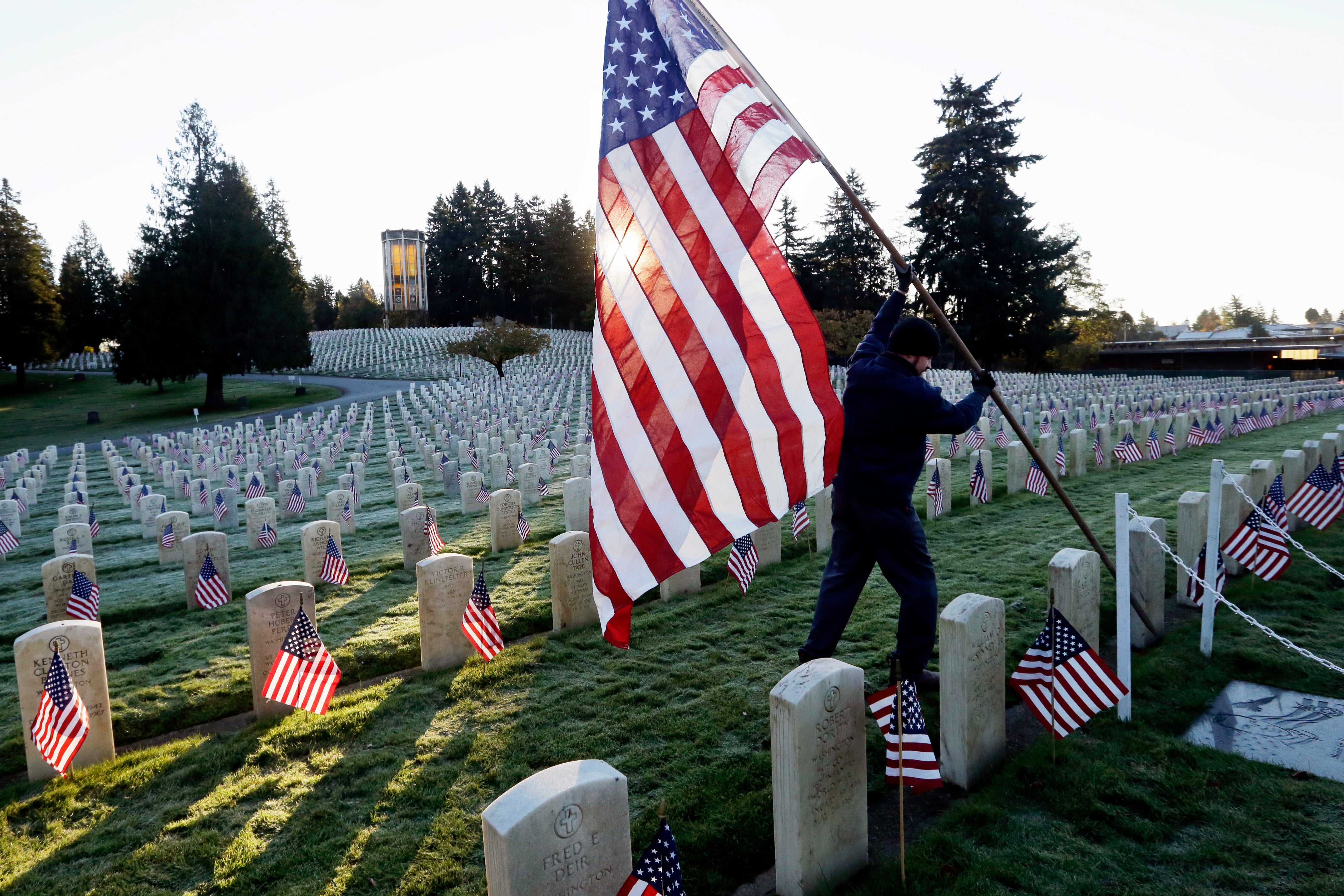 A large American flag is raised among flag-covered graves on Veterans Day in the veterans' section of Evergreen-Washelli cemetery in Seattle