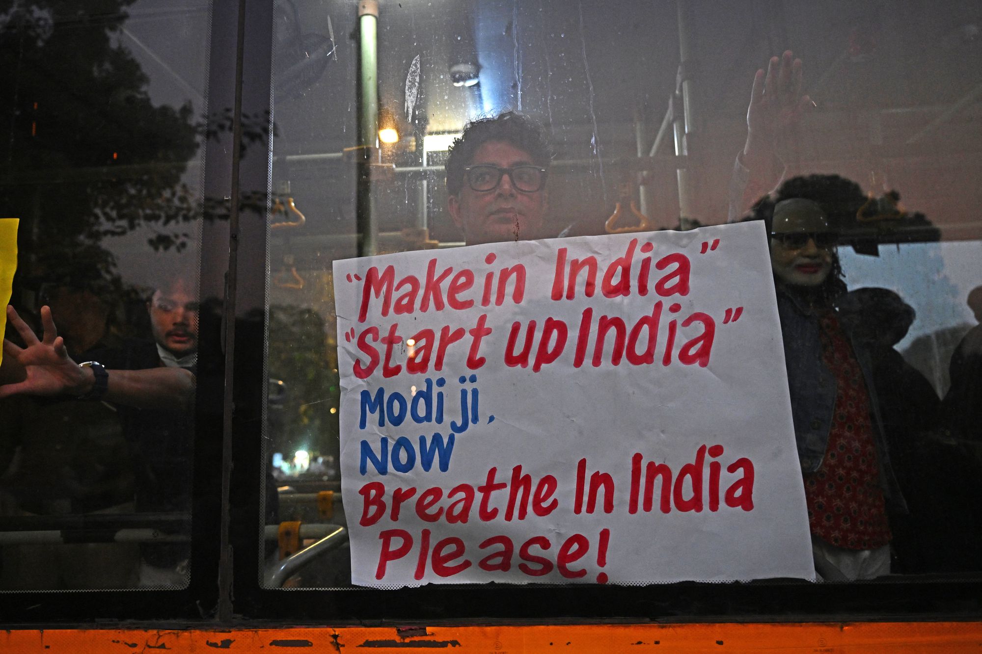 A detained protester holds a placard from inside a police vehicle
