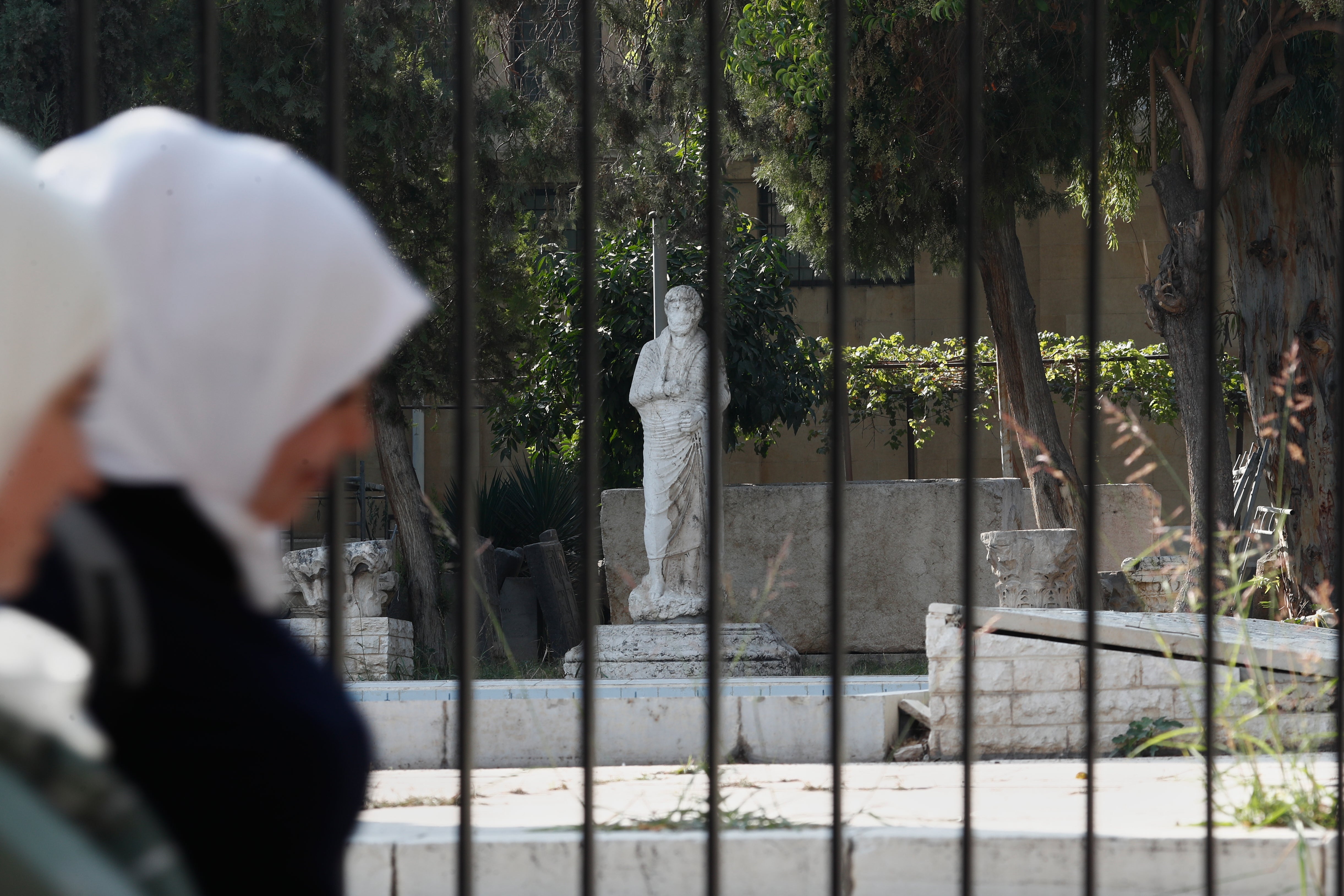 <p>Syrian women walk past a fence of the National Museum of Syria in Damascus, Syria, where the treasures were stolen from</p>