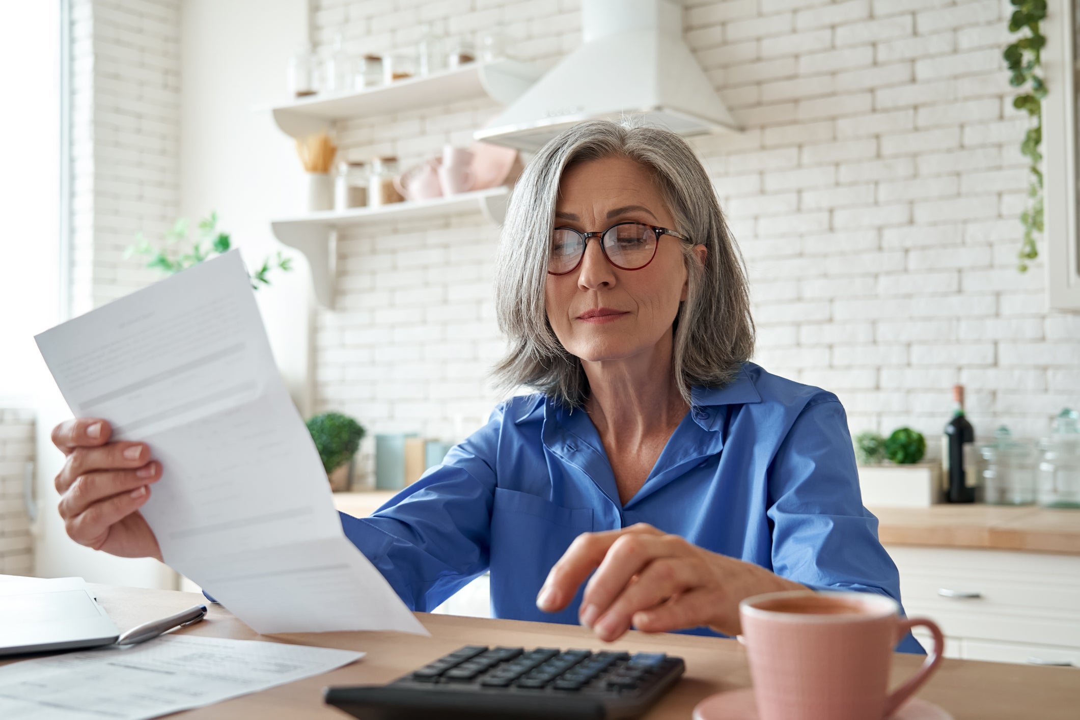 <p>Woman looking at paperwork in front of computer</p>