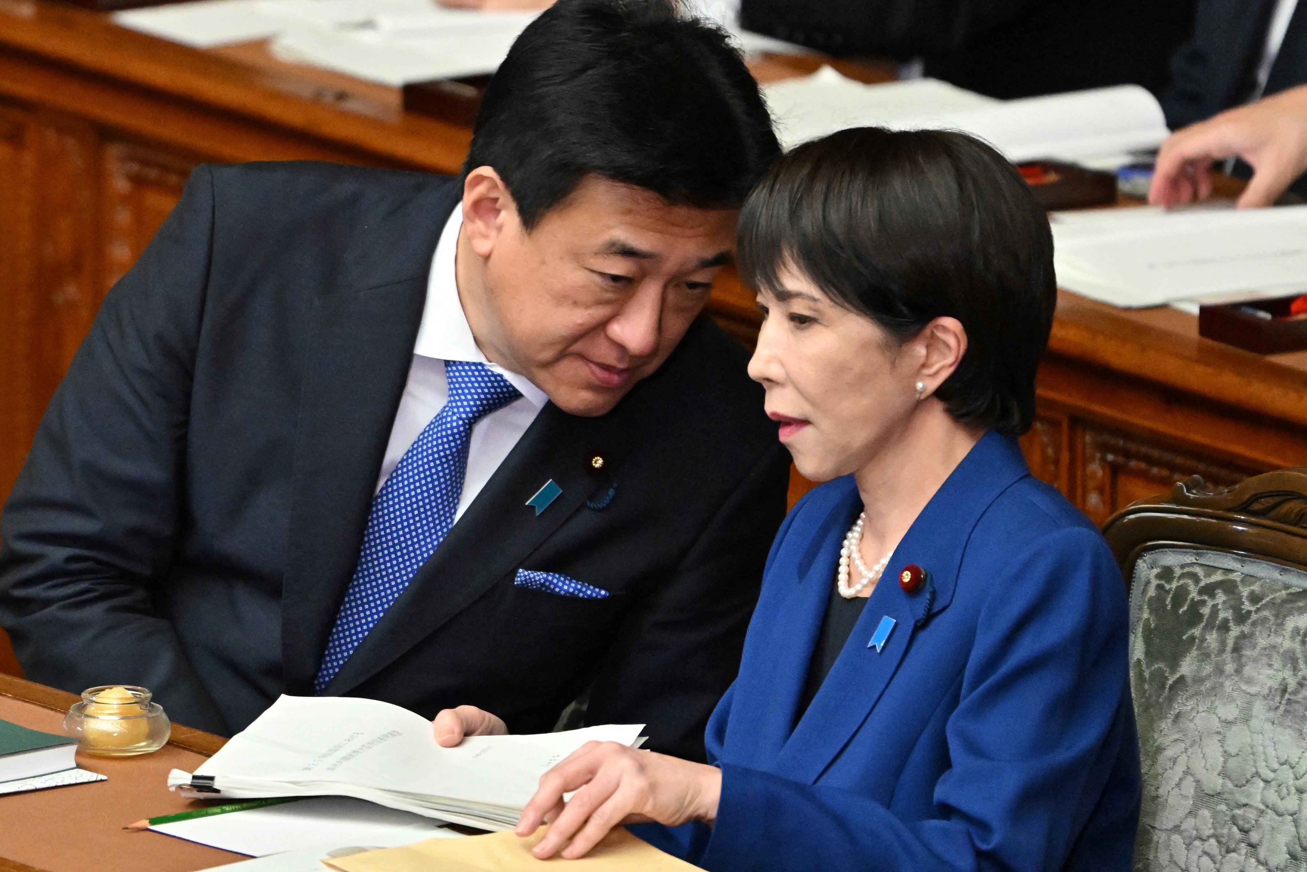 Japan's prime minister Sanae Takaichi (R) chats with chief cabinet secretary Minoru Kihara after delivering her policy speech