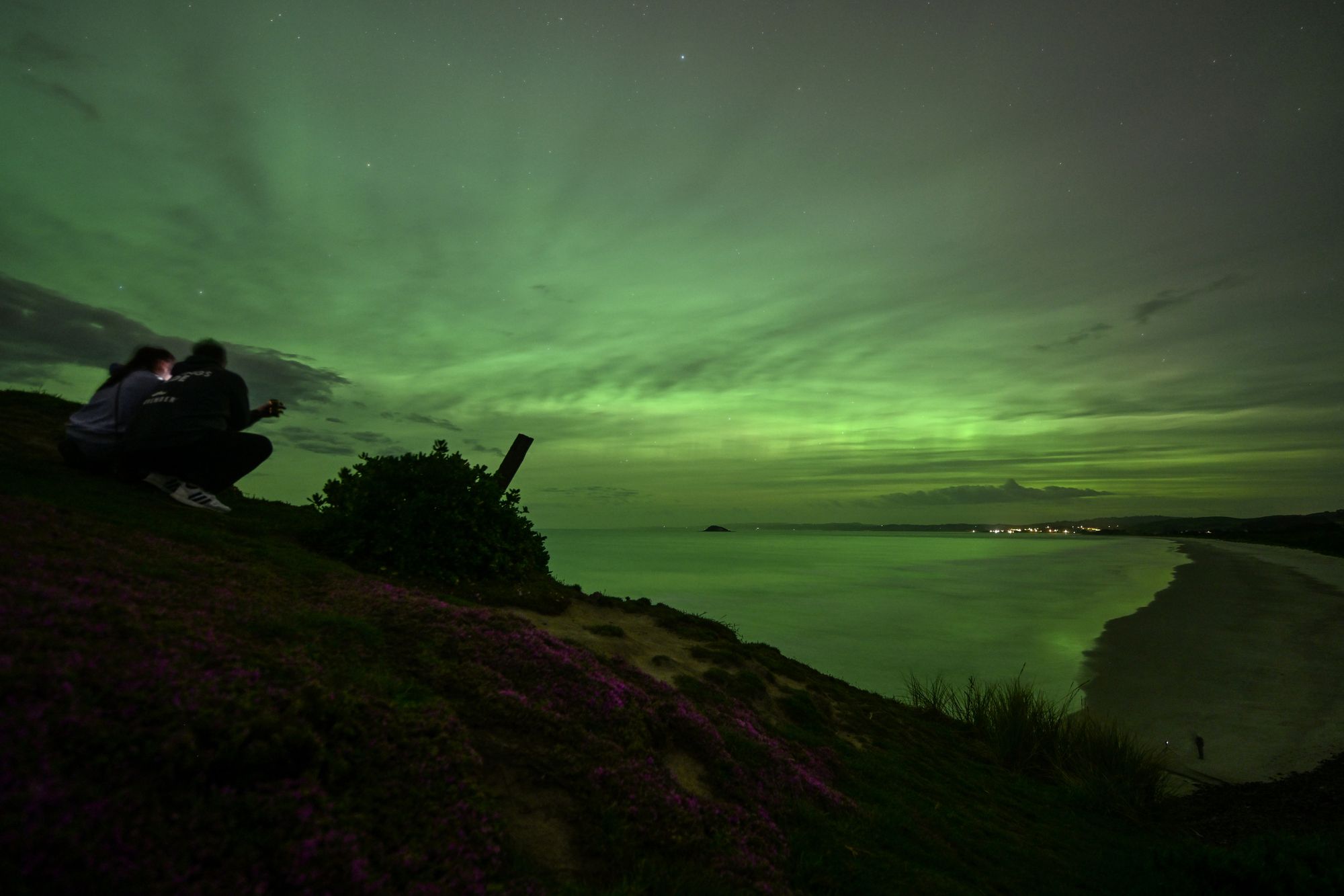 People take pictures of the Aurora Australis, also known as the Southern Lights, as it glows on the horizon over the waters of Blackhead Beach in Dunedin on November 13, 2025