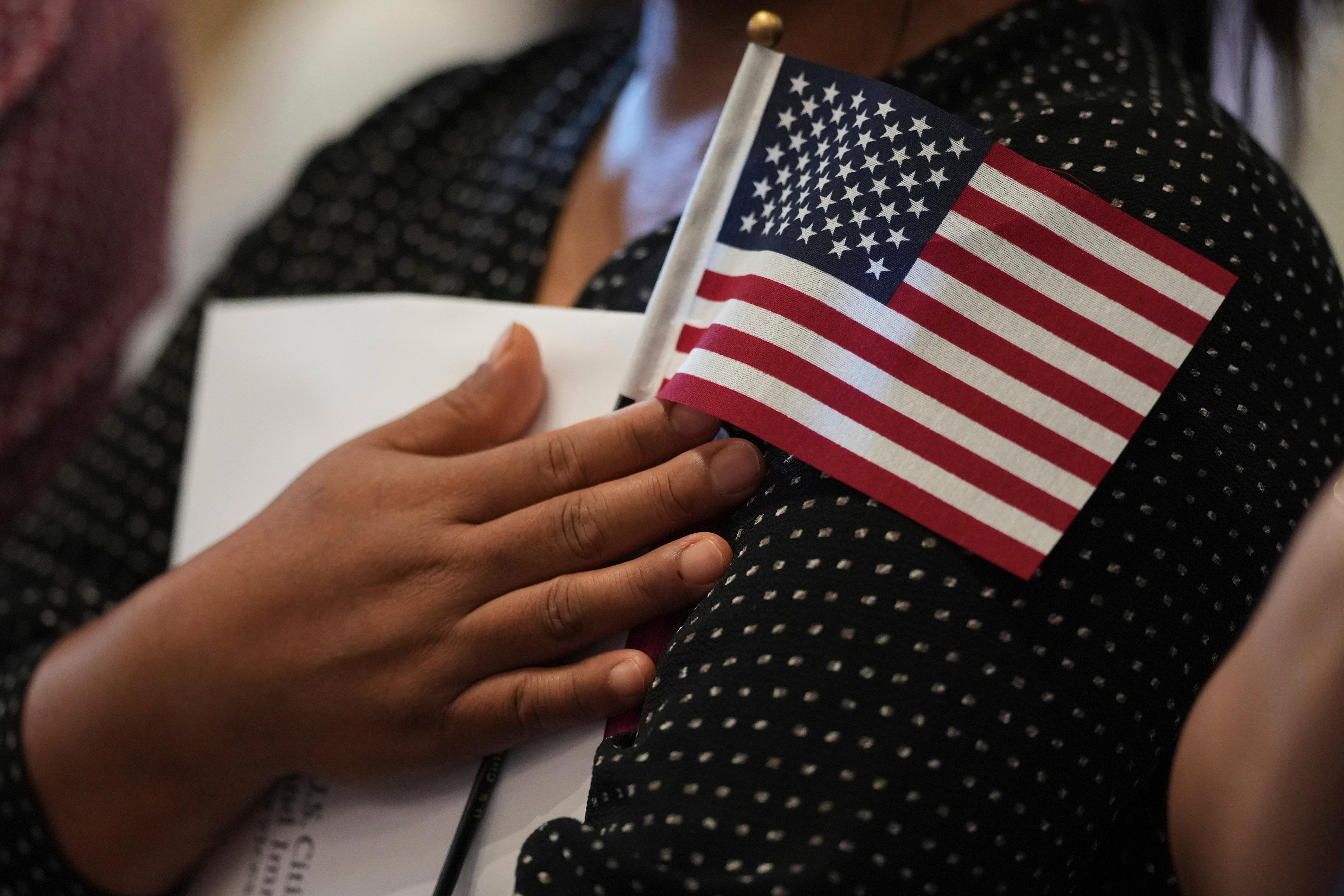 A woman clutches a U.S. flag as she and applicants from other countries prepare to take the oath of citizenship in commemoration of Independence Day during a Naturalization Ceremony in San Antonio