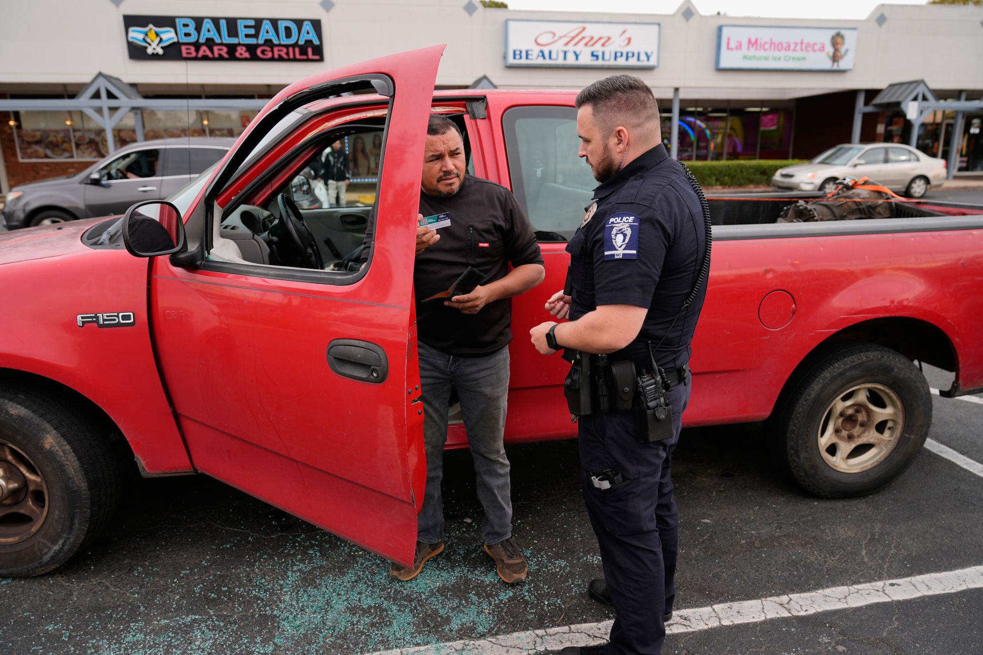 Willy Aceituno, left, makes a police report with a Charlotte-Mecklenburg Police Department officer after Border Patrol officers broke his window during an enforcement operation November 15