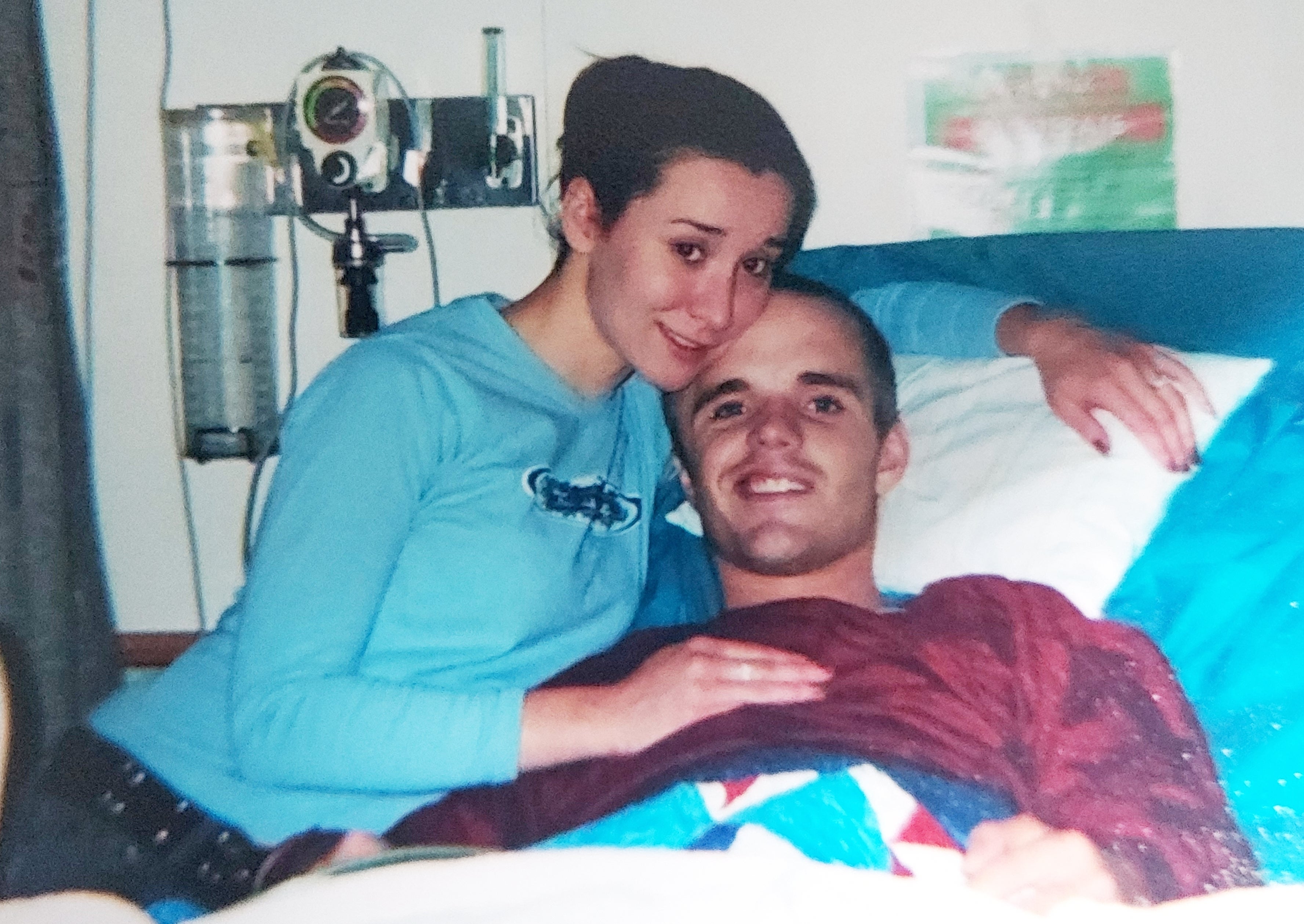 Nigel Max Edge, then known as Sean DeBevoise, lies in a hospital bed next to his wife, Rachel Crowl, in Bethesda, Md.
