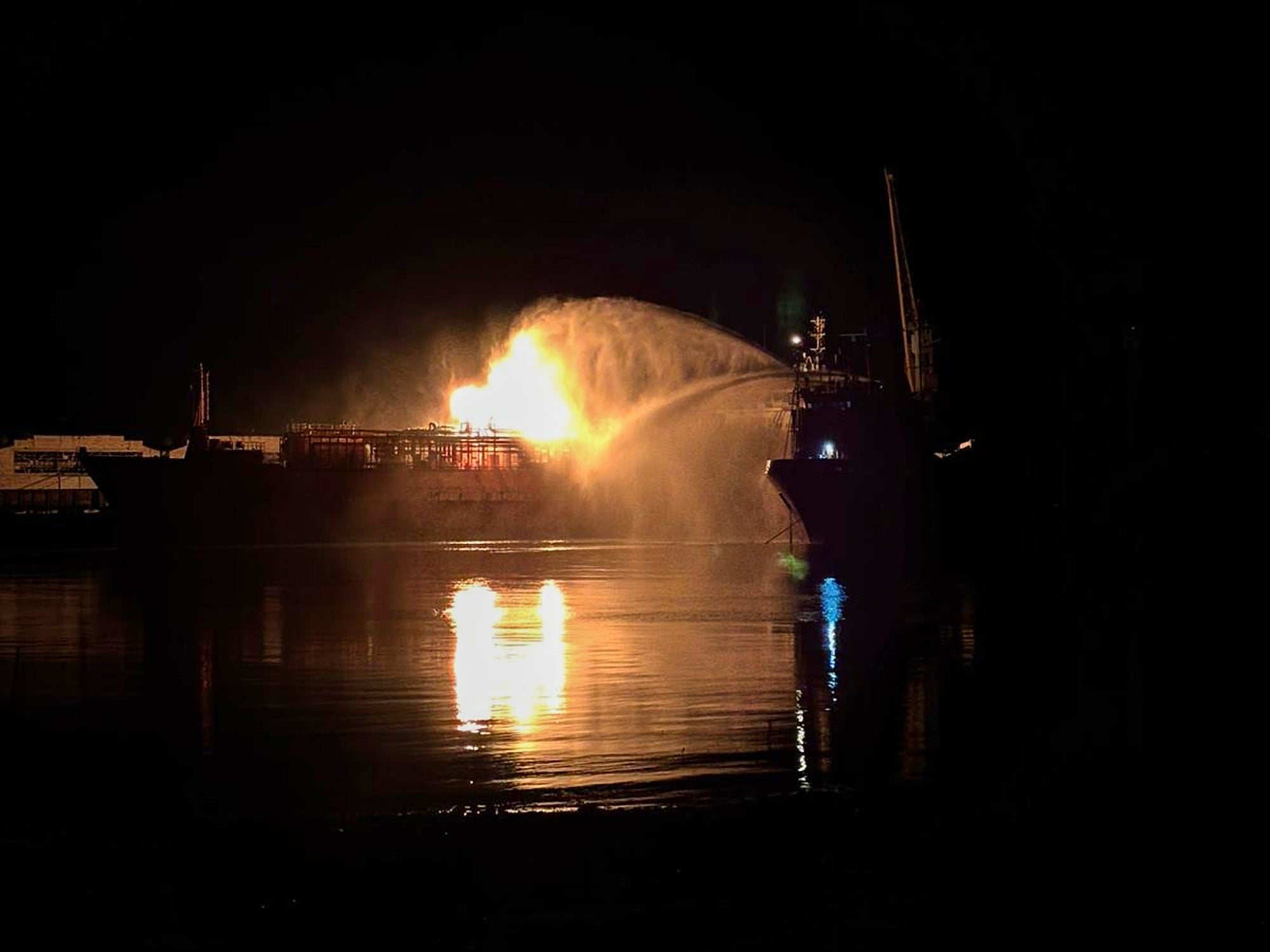 A Ukrainian vessel spraying water on a cargo ship loaded with liquified petroleum gas engulfed by flames following Russian strikes, early Monday