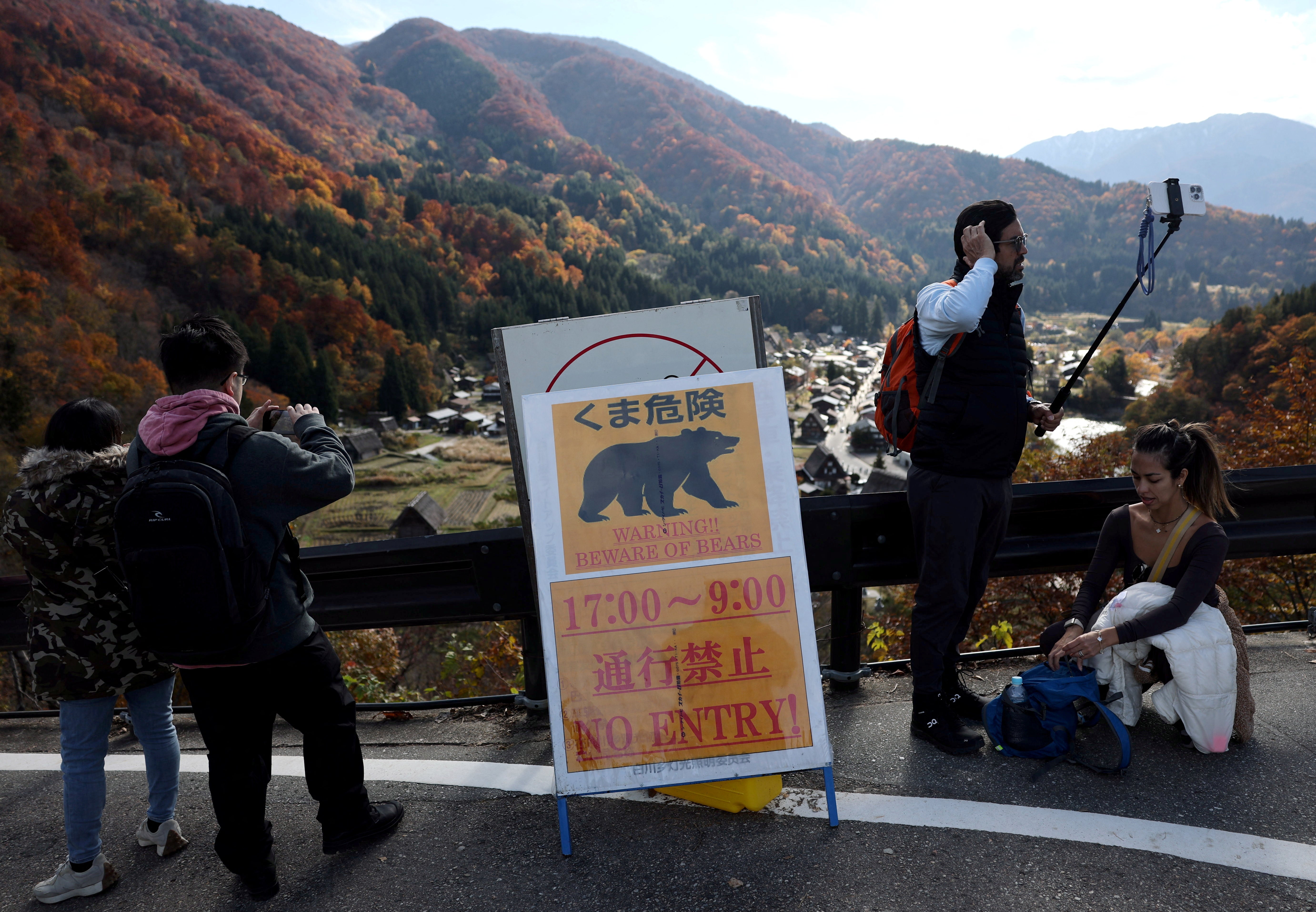 Visitors take souvenir photos next to a bear warning sign at Shirakawa-go, a popular tourist spot and one of Japan's UNESCO World Heritage sites, in Shirakawa village, Gifu Prefecture, Japan