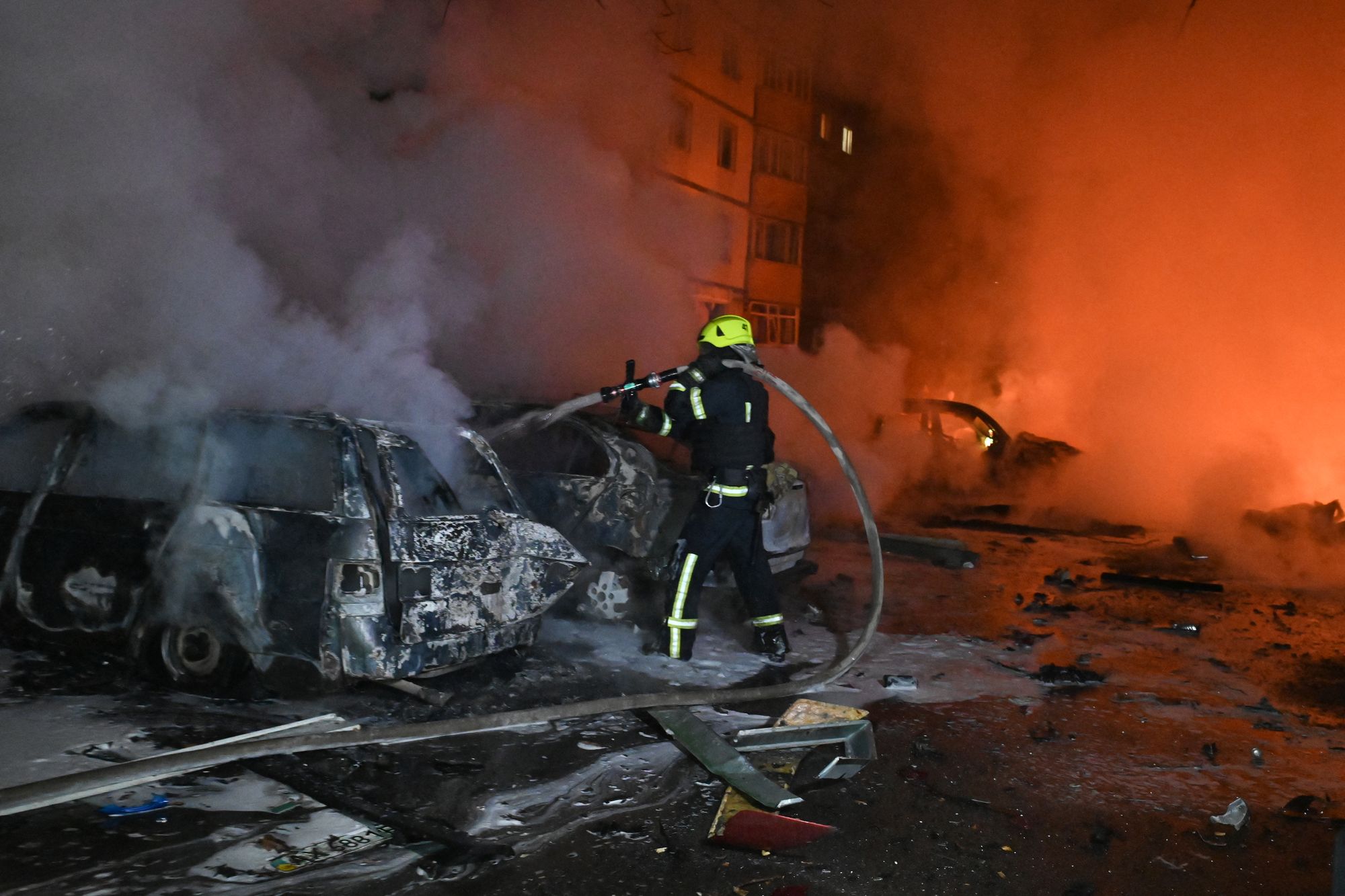 A Ukrainian firefighter uses a water hose to extinguish a fire at the site of a Russian strike in Kharkiv