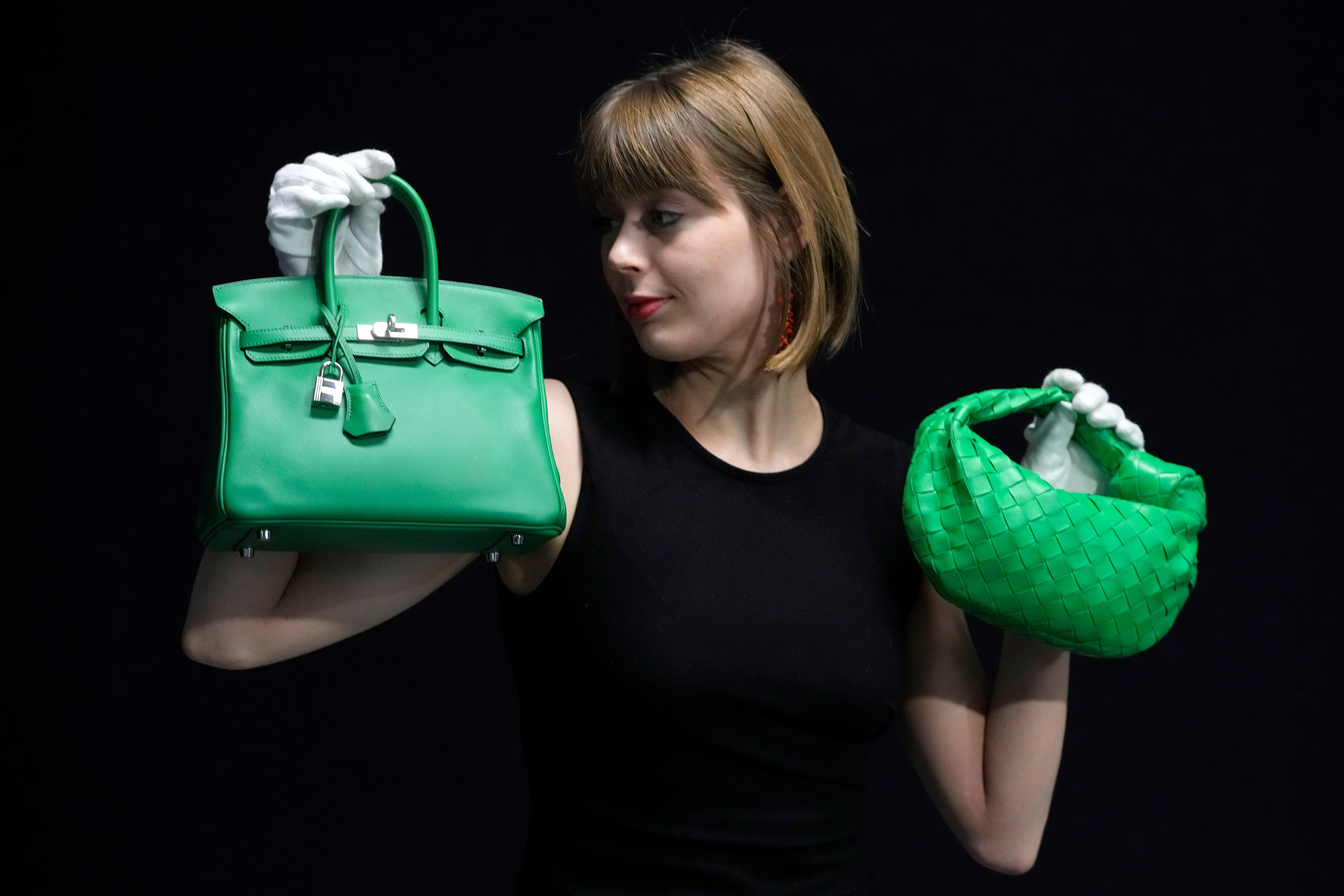 FILE - A Bonhams employee displays a Hermes: a Bambou Swift Leather Birkin 25 bag, left, and a Bottega Veneta: a Parakeet Green Lambskin Mini Jodie, right, at the auction rooms in London on Feb. 26, 2024