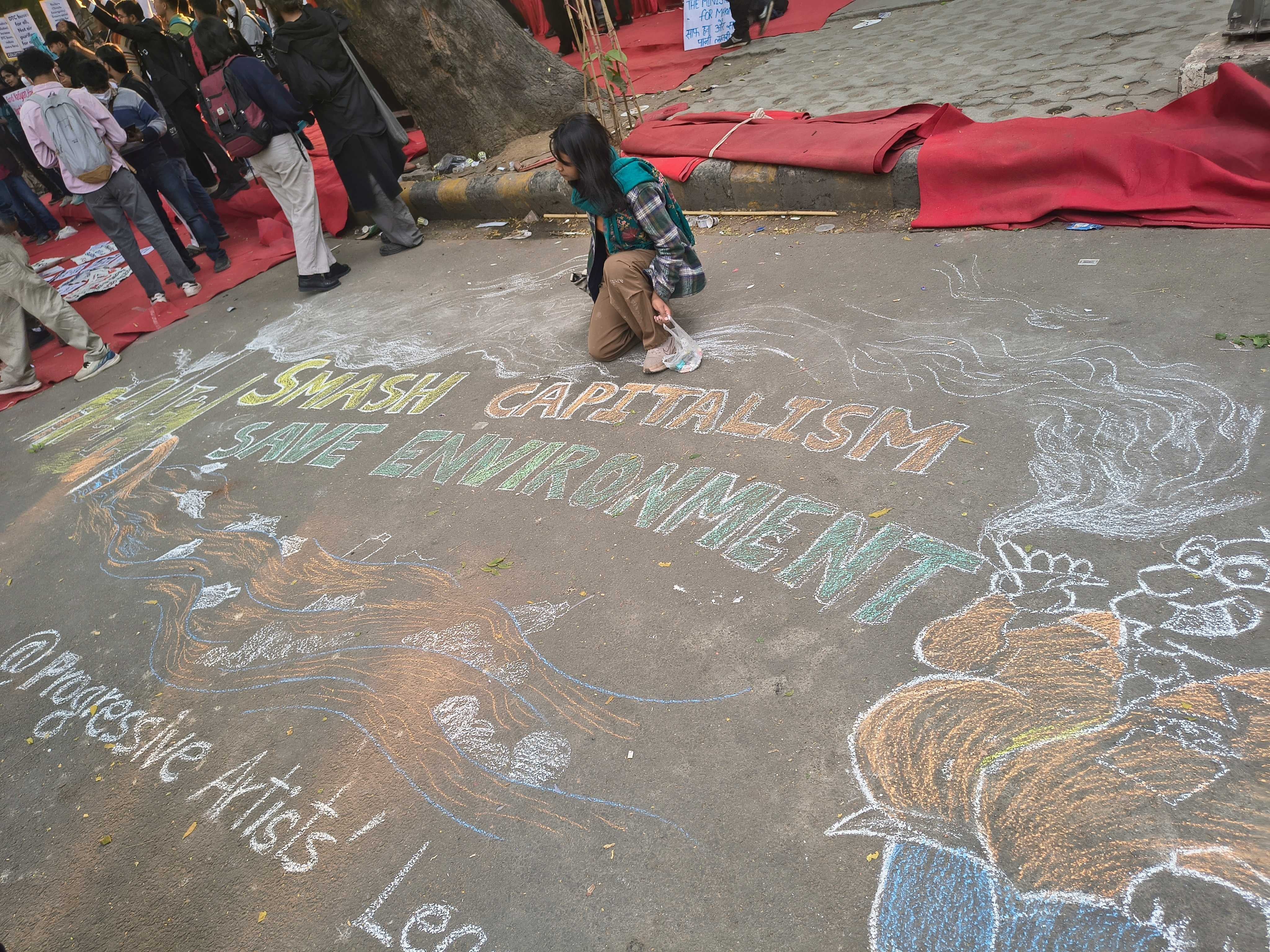 A volunteer draws a chalk mural reading ‘Smash capitalism, save environment’ during the protest