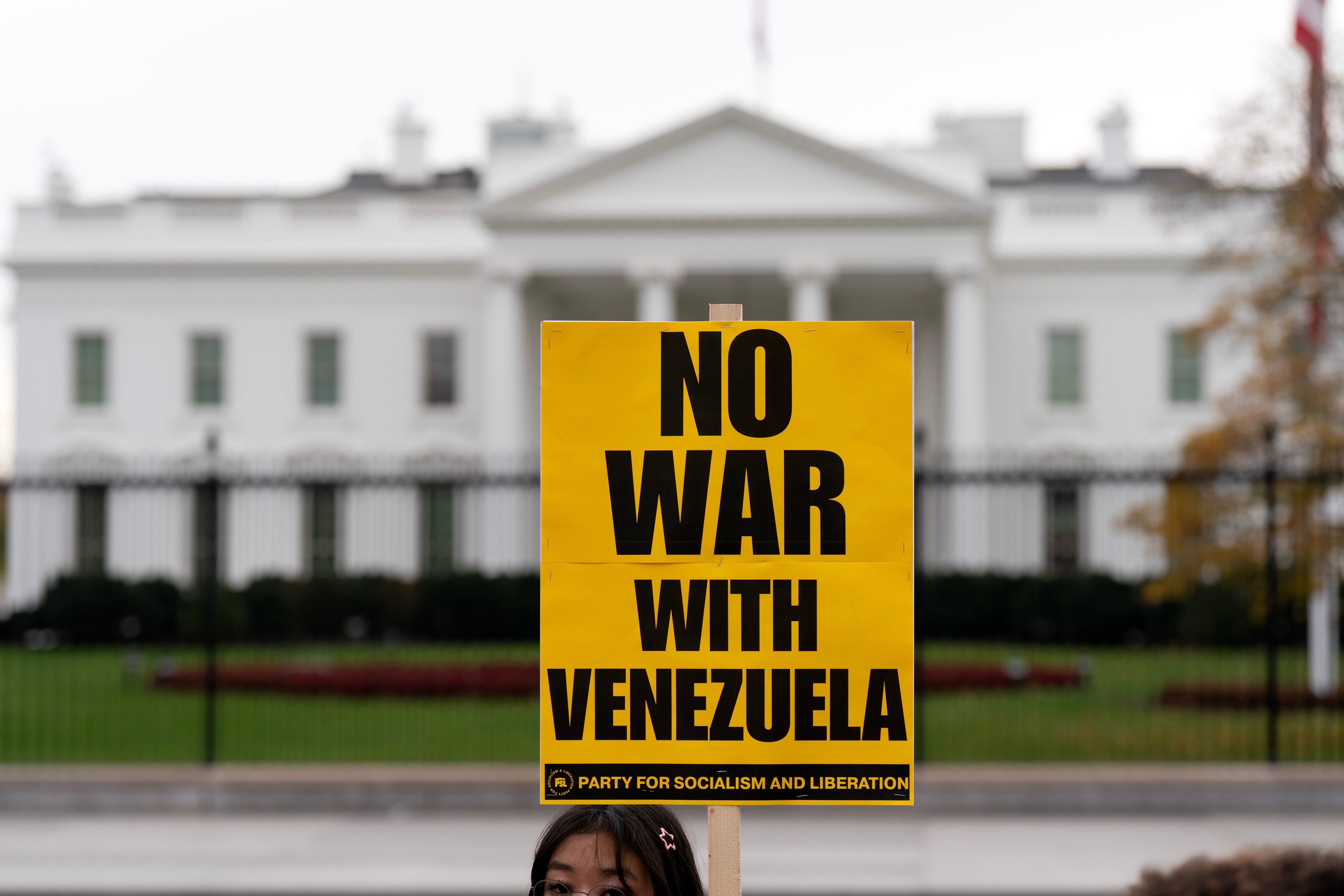 A protester carries a sign opposing a U.S. war with Venezuela outside the White House in Washington, D.C. on November 15, 2025. A CBS/YouGov poll found that 70 percent of Americans opposed military action in Venezuela