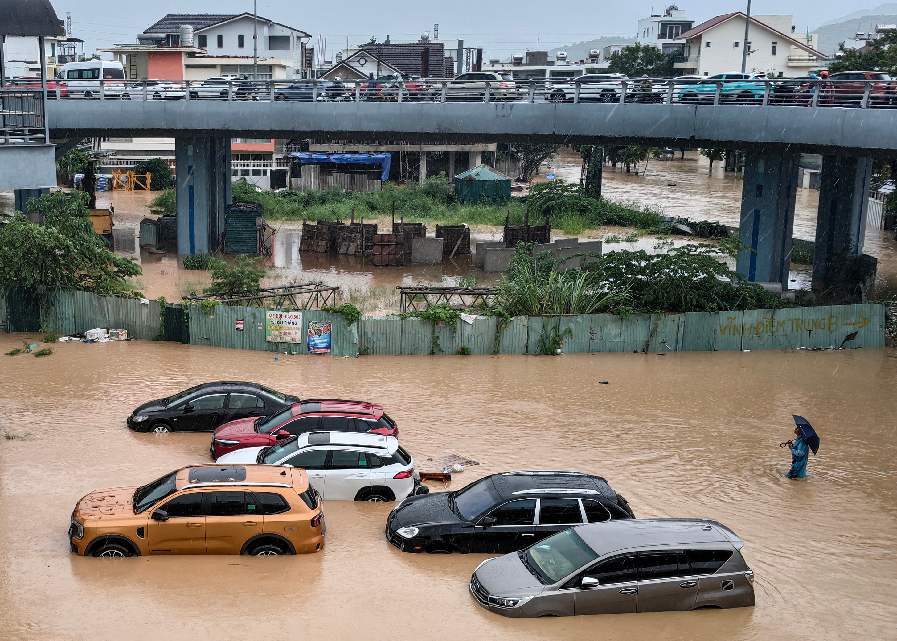 <p>A man (R) wades through floodwaters near inundated vehicles in Nha Trang, Vietnam's coastal province of Khanh Hoa on November 20, 2025</p>