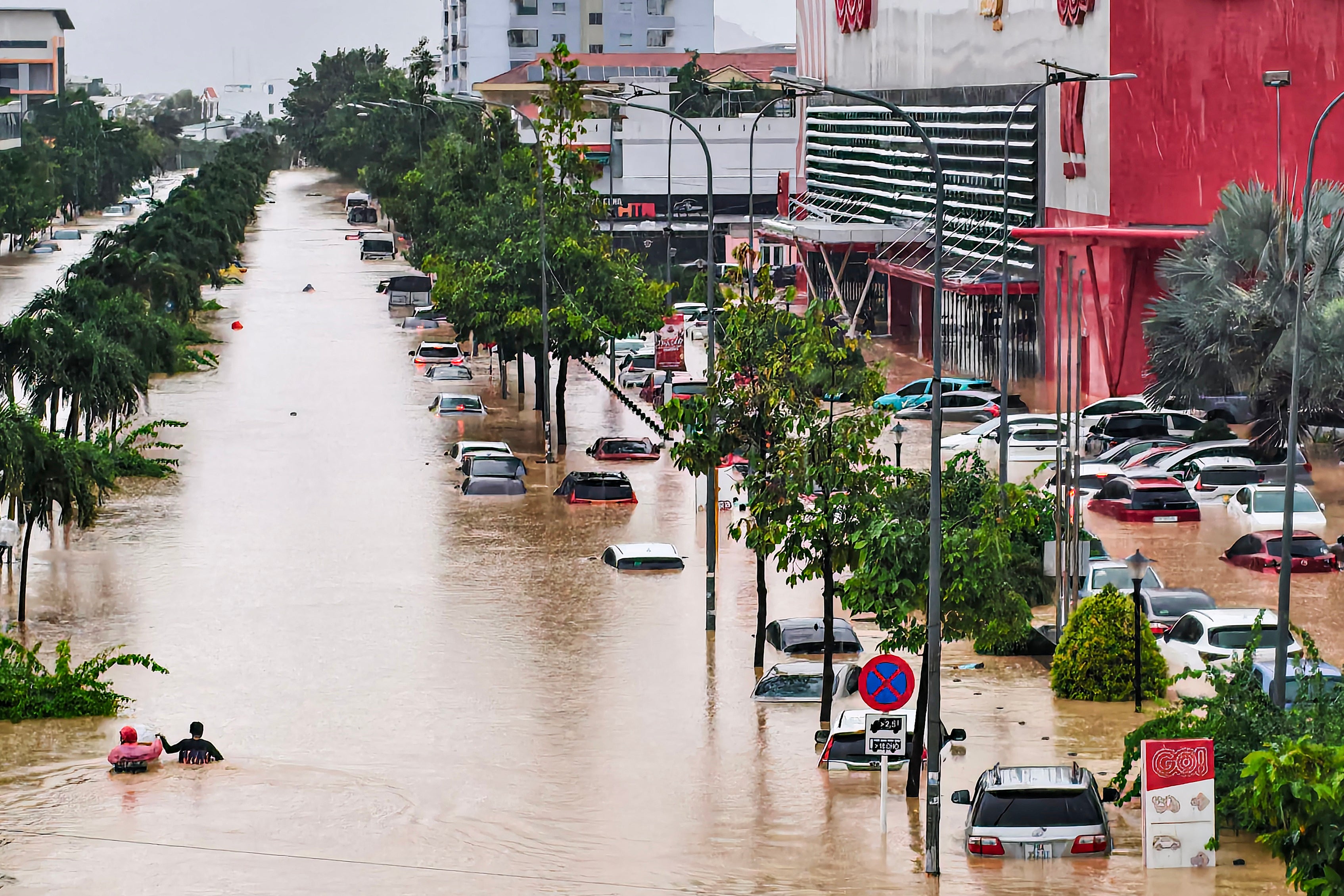 People (L) wade through floodwaters near inundated vehicles in Nha Trang, Vietnam's coastal province of Khanh Hoa on November 20, 2025. The death toll from a week of torrential rain that triggered floods and landslides in central Vietnam has risen to 16 while thousands of homes inundated in "historic" floodings, authorities said. (Photo by Duc Thao / AFP) (Photo by DUC THAO/AFP via Getty Images)