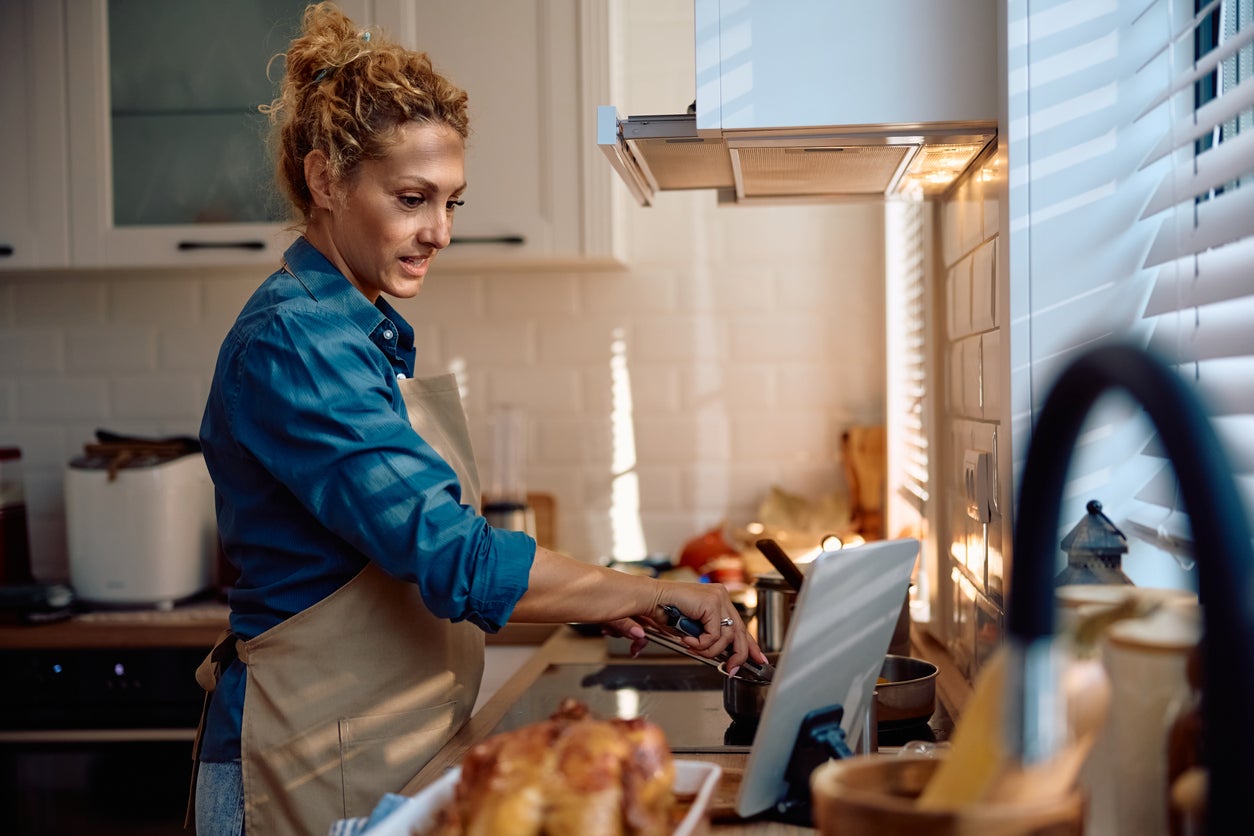 <p>Smiling woman cooking Thanksgiving meal while following recipe on digital tablet in the kitchen.</p>