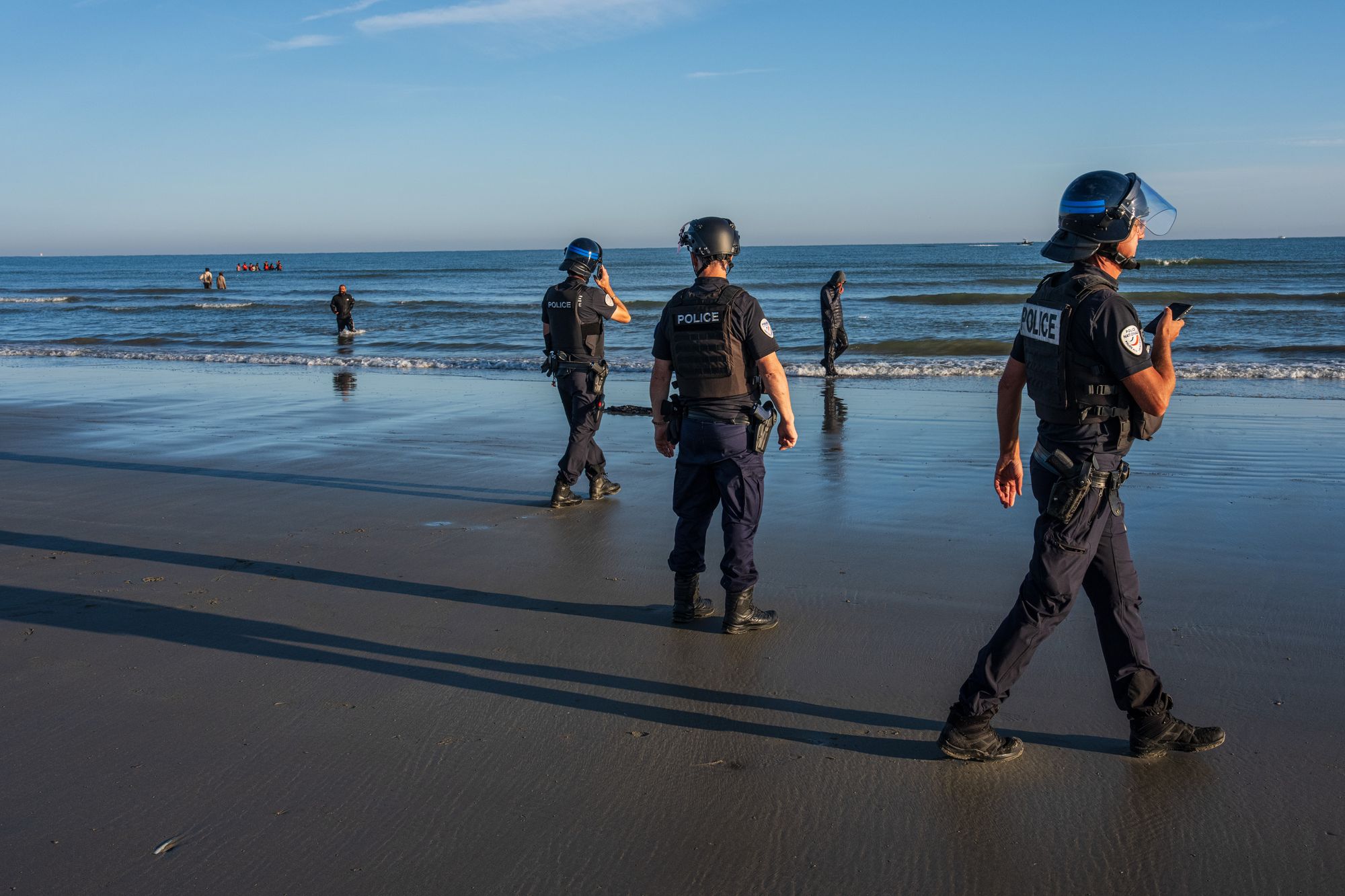 Migrants walk past French police officers after failing to board a dinghy to cross the English Channel