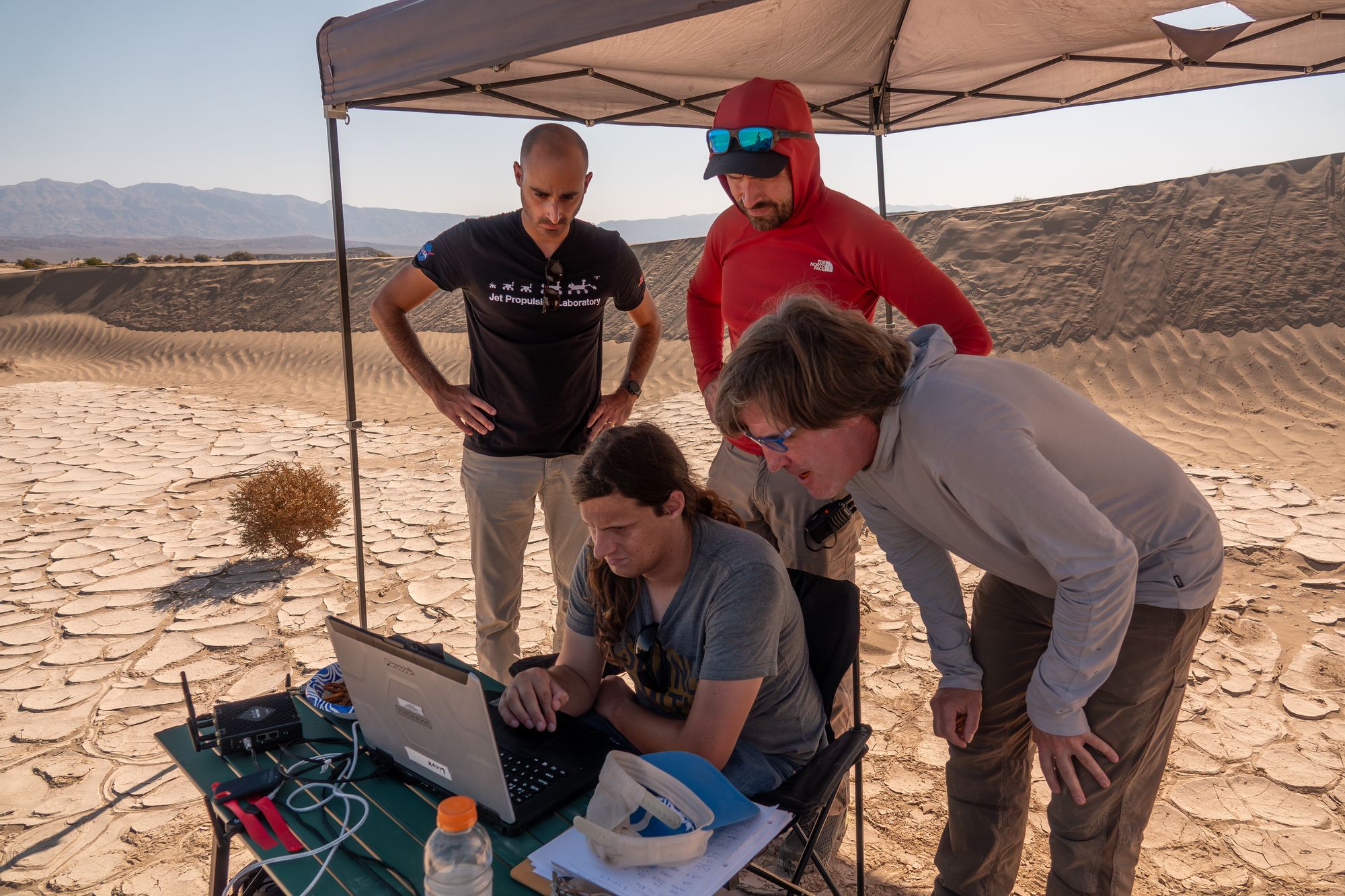 Researchers gather under a tent in Death Valley National Park while monitoring a research drone