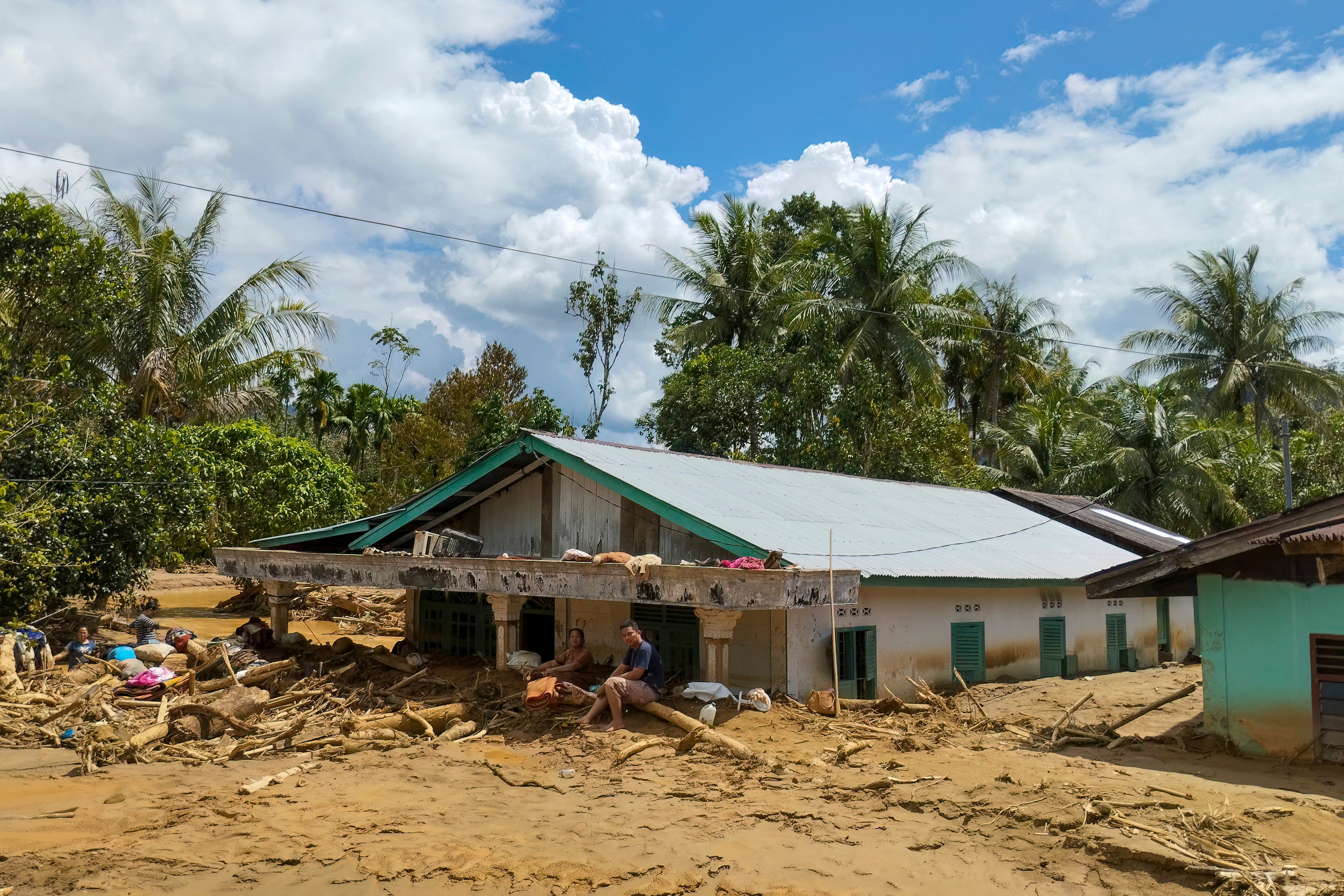 A couple sits in front of their house, which is half-submerged in mud following a flash flood that struck their village in Tukka, Central Tapanuli Regency, North Sumatra province