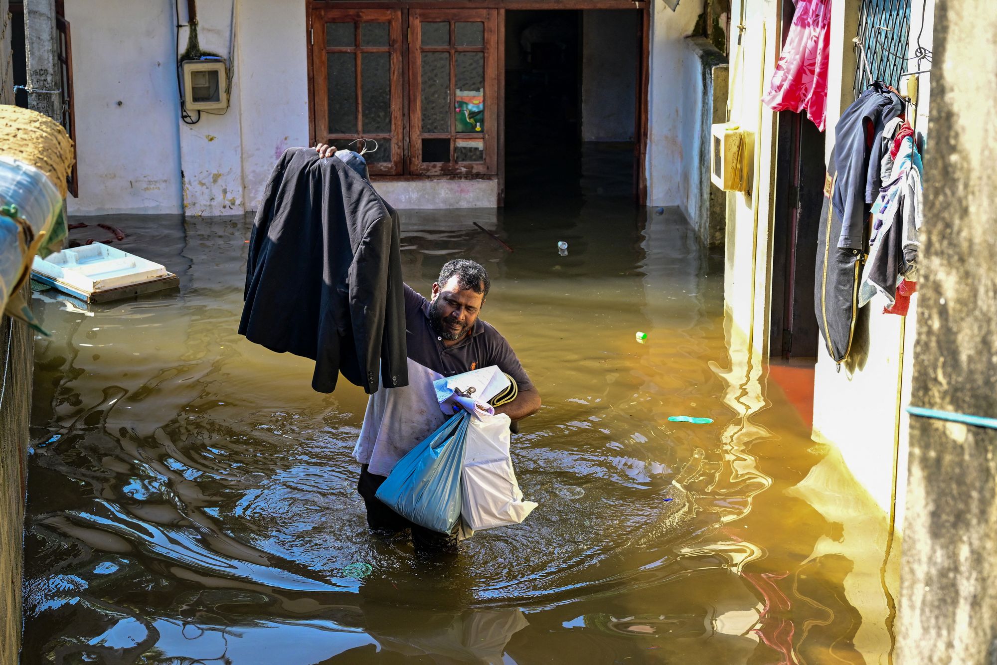 A man with his belongings wades through floodwaters outside his house in Wellampitiya on the outskirts of Colombo on November 30, 2025