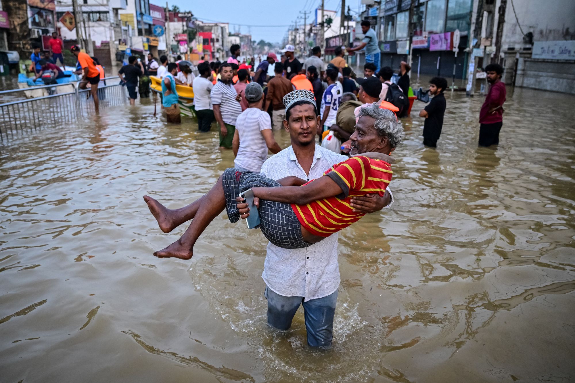 A youth carries an elderly man as they wade through a flooded street after heavy rainfall in Wellampitiya on the outskirts of Colombo on November 30, 2025