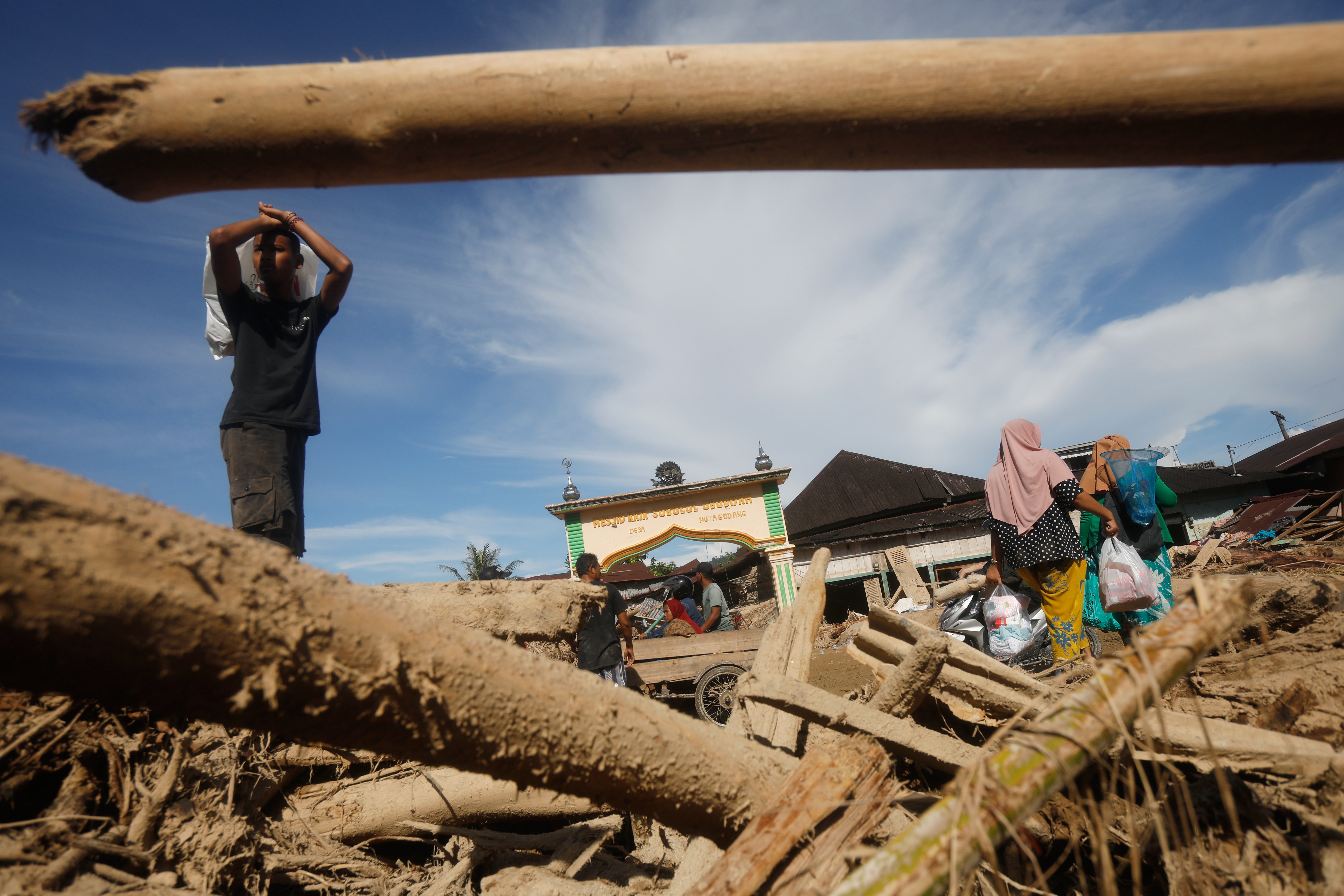 Survivors walk past logs swept away by a flash flood in Batang Toru, North Sumatra, Indonesia