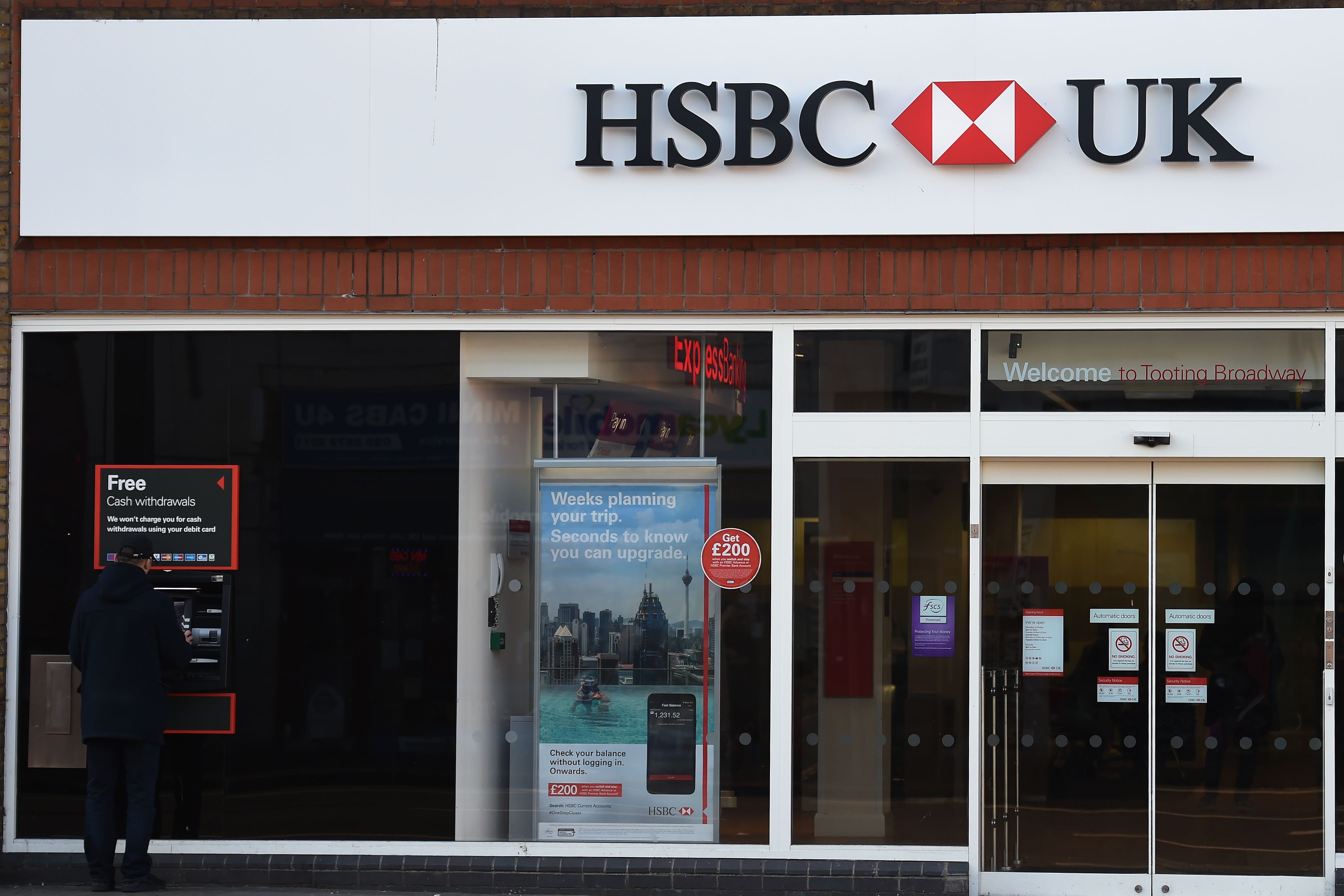A customer uses a cash machine at a branch of HSBC in Tooting Broadway, London