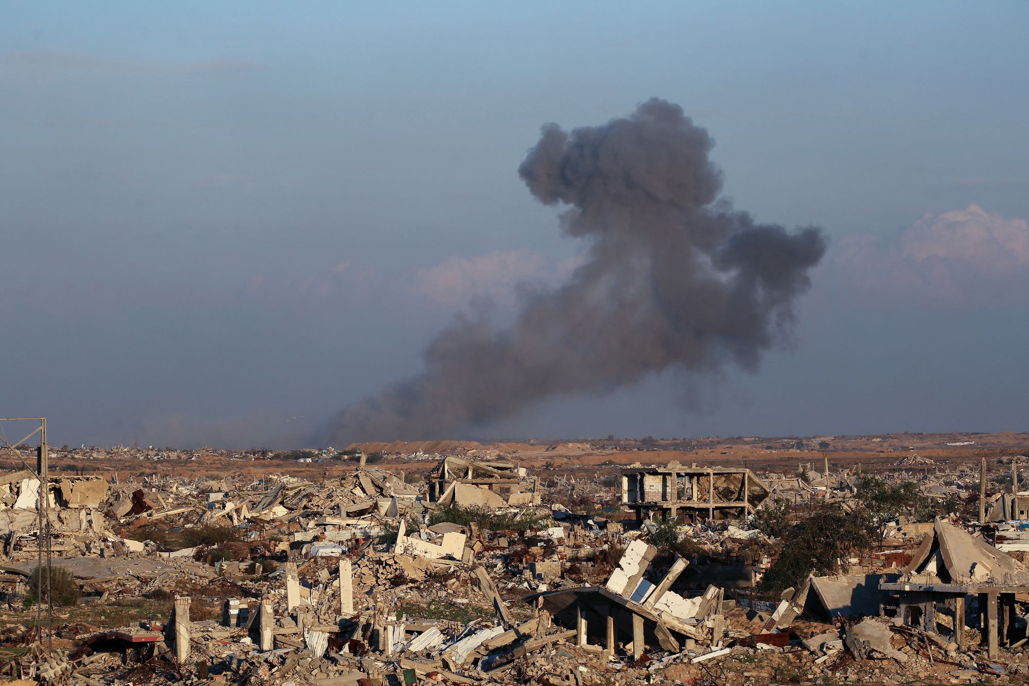 This picture taken from the Nuseirat camp for displaced Palestinians shows destroyed buildings and smoke billowing in the distance following Israeli strikes east of Gaza City on December 2, 2025