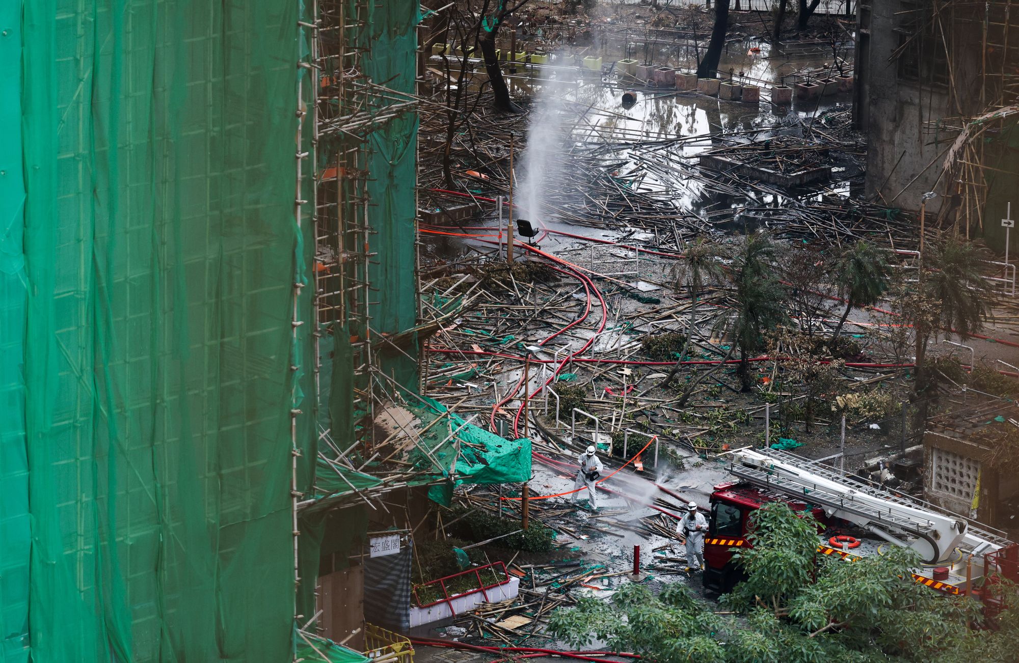 Police officers wearing personal protective equipment walk among debris of bamboo scaffoldings and protective netting by the buildings of the Wang Fuk Court housing complex after the deadly fire, in Tai Po, Hong Kong, China, 3 December 2025