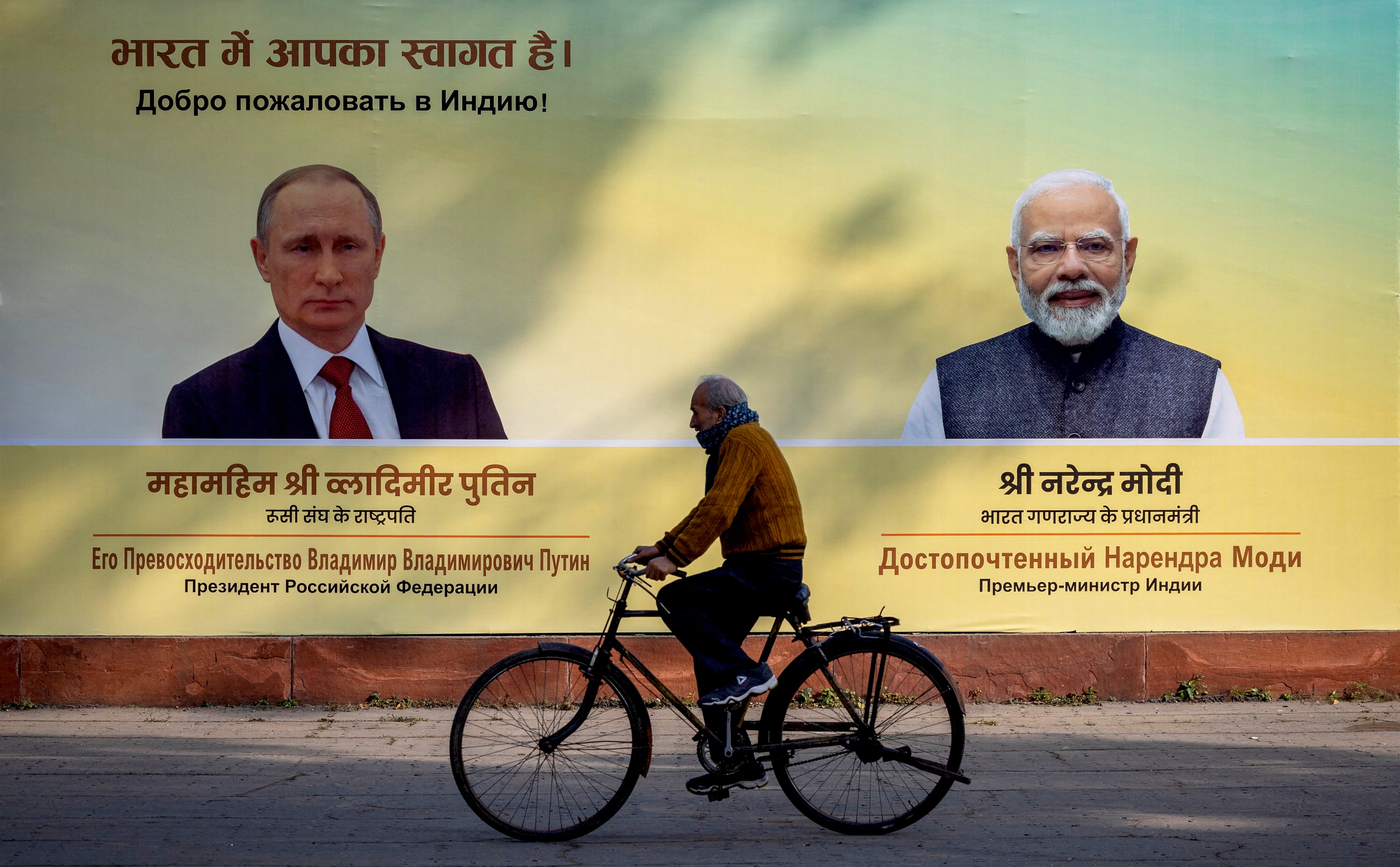 A man cycles past a hoarding with images of Vladimir Putin and Narendra Modi in Delhi on 4 December 2025