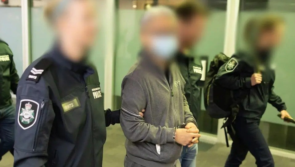File. Photo released by Australian police shows officers escorting Tse Chi Lop through the Melbourne airport after he was extradited from the Netherlands on 22 December 2022