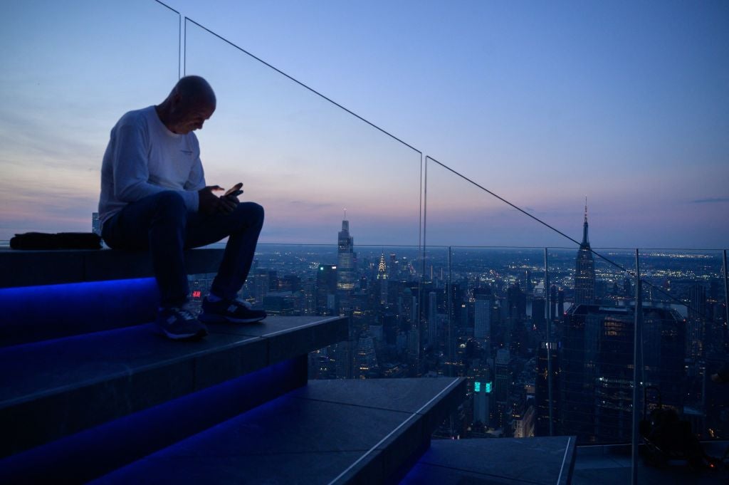 A man looks at a mobile phone as he sits before the Manhattan skyline on June 10, 2021. A new study examined 10 of the leading credit card issuers in the country based on four categories and five tasks. In addition to Bank of America, the study included American Express , Barclays US, Capital One, Chase, Citibank, Discover, PNC, US Bank, and Wells Fargo.