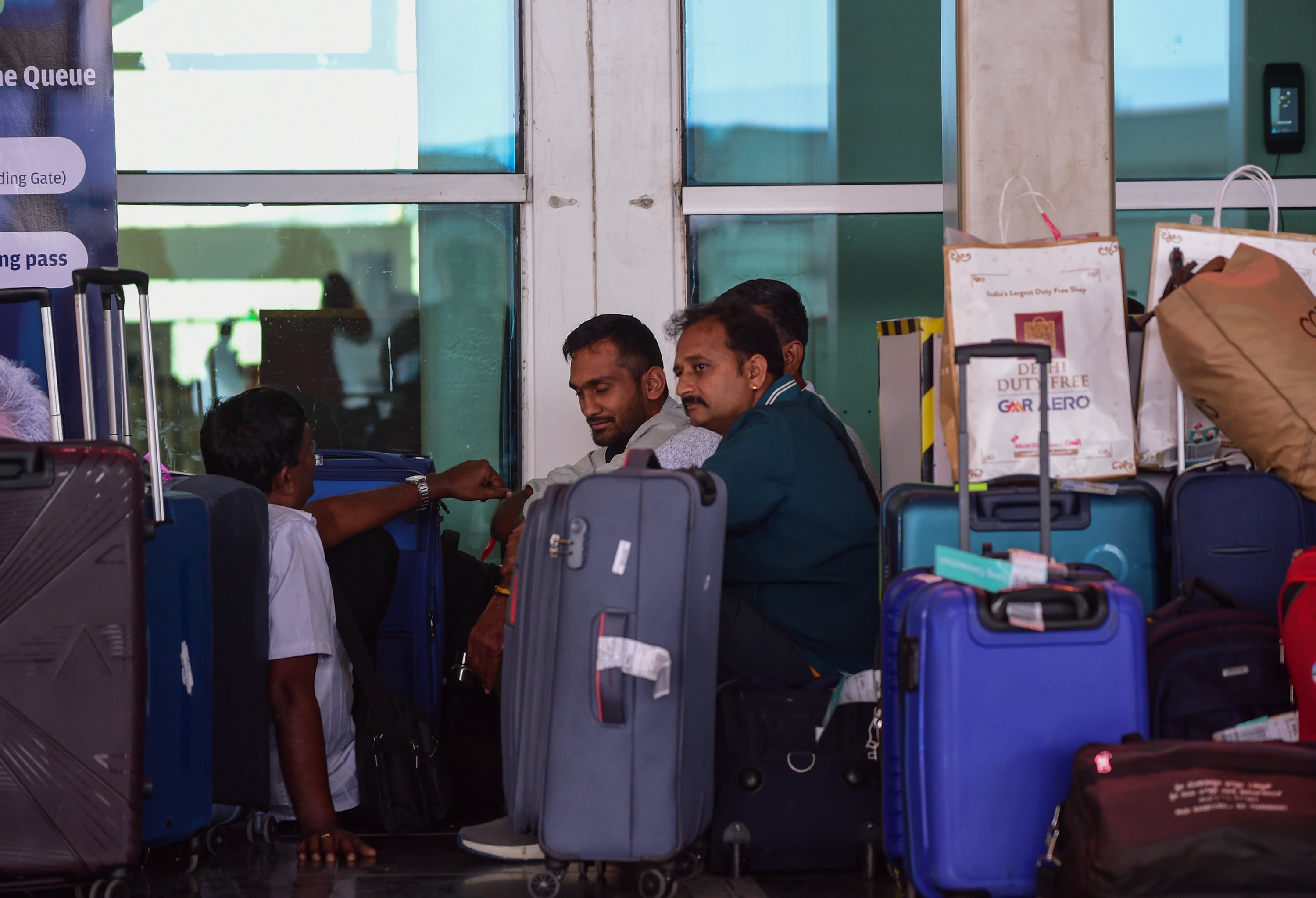 Passengers sit outside of Terminal 1 of Indira Gandhi International Airport after mass cancellation of Indigo flights on December 05, 2025 in New Delhi, India