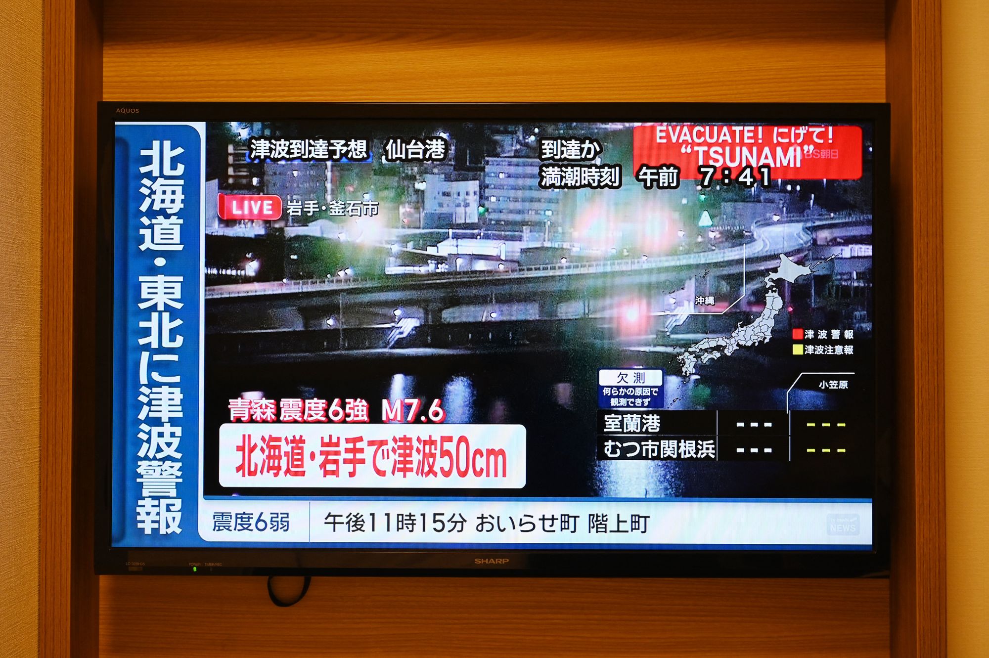 A tsunami warning flashes over live footage of a waterfront area, on a television screen in Sapporo, in Japan's northern Hokkaido prefecture on December 9, 2025