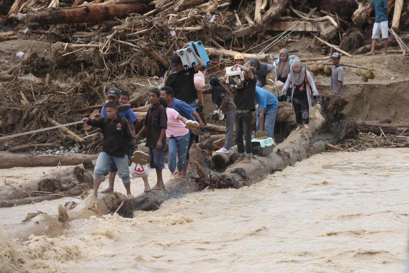 Flood survivors use logs to cross a river in Batang Toru, North Sumatra, Indonesia
