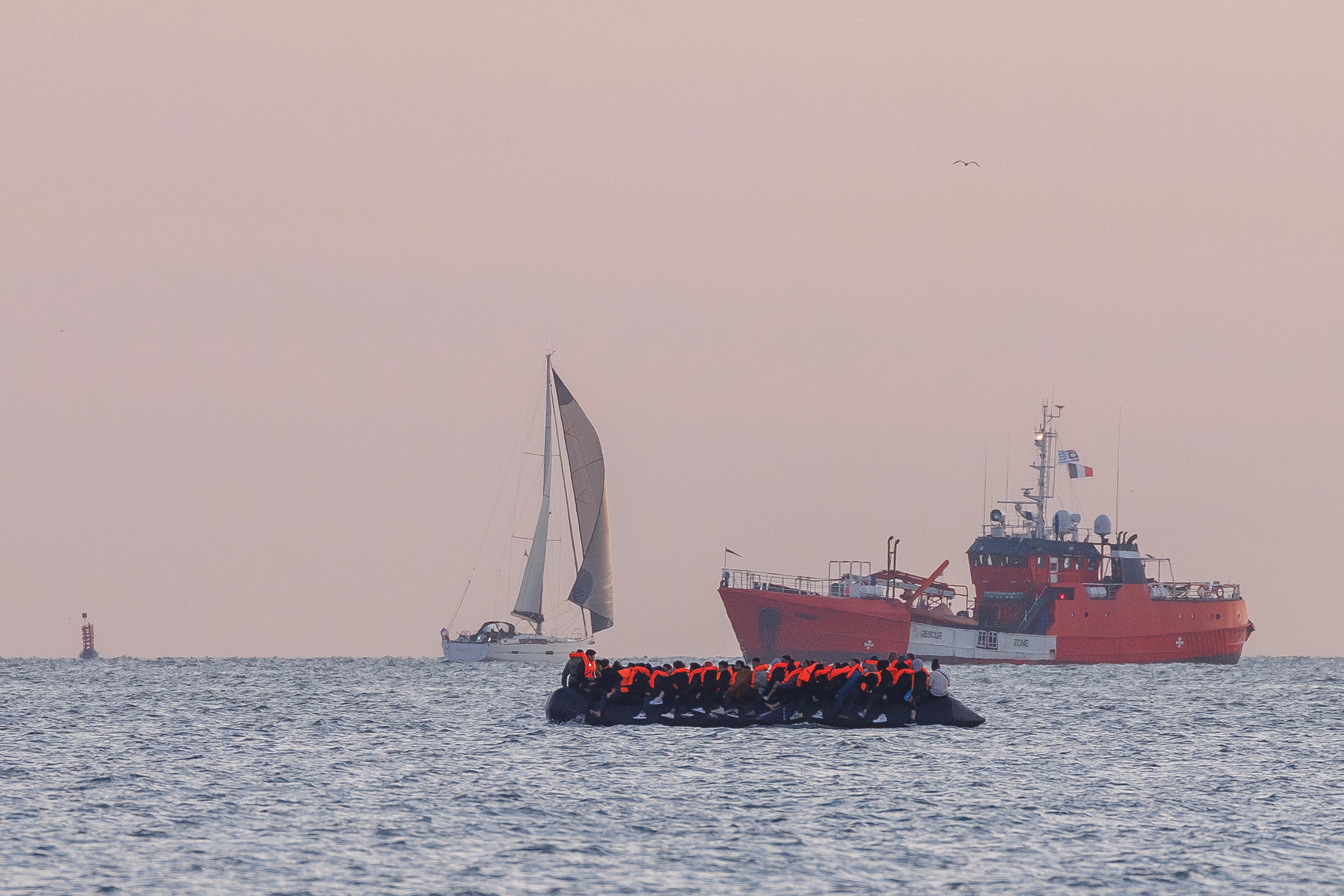 A search and rescue vessel shadows a small boat carrying migrants as it sets off from the coast into the Channel, heading for the UK on August 15, 2025 in Gravelines, France.