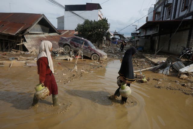 <p>Survivors walk past the wreckage of a car at an area affected by flash flooding in the aftermath of Cyclone Senyar in Aceh Tamiang, on Sumatra Island, Indonesia</p>