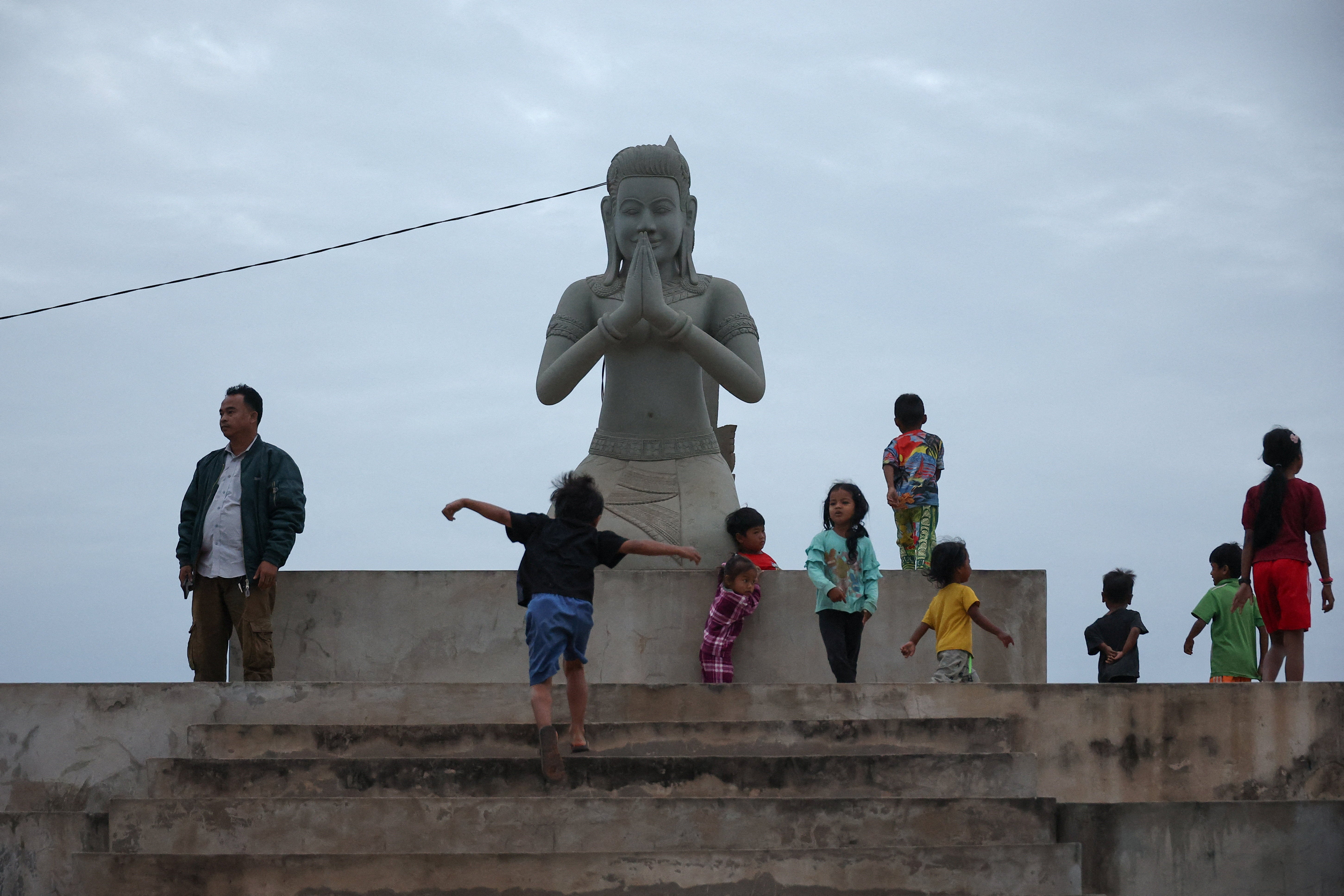 Children play near a statue at a refugee camp after evacuation, amid deadly clashes between Thailand and Cambodia along a disputed border area, in Srei Snam, Siem Reap Province