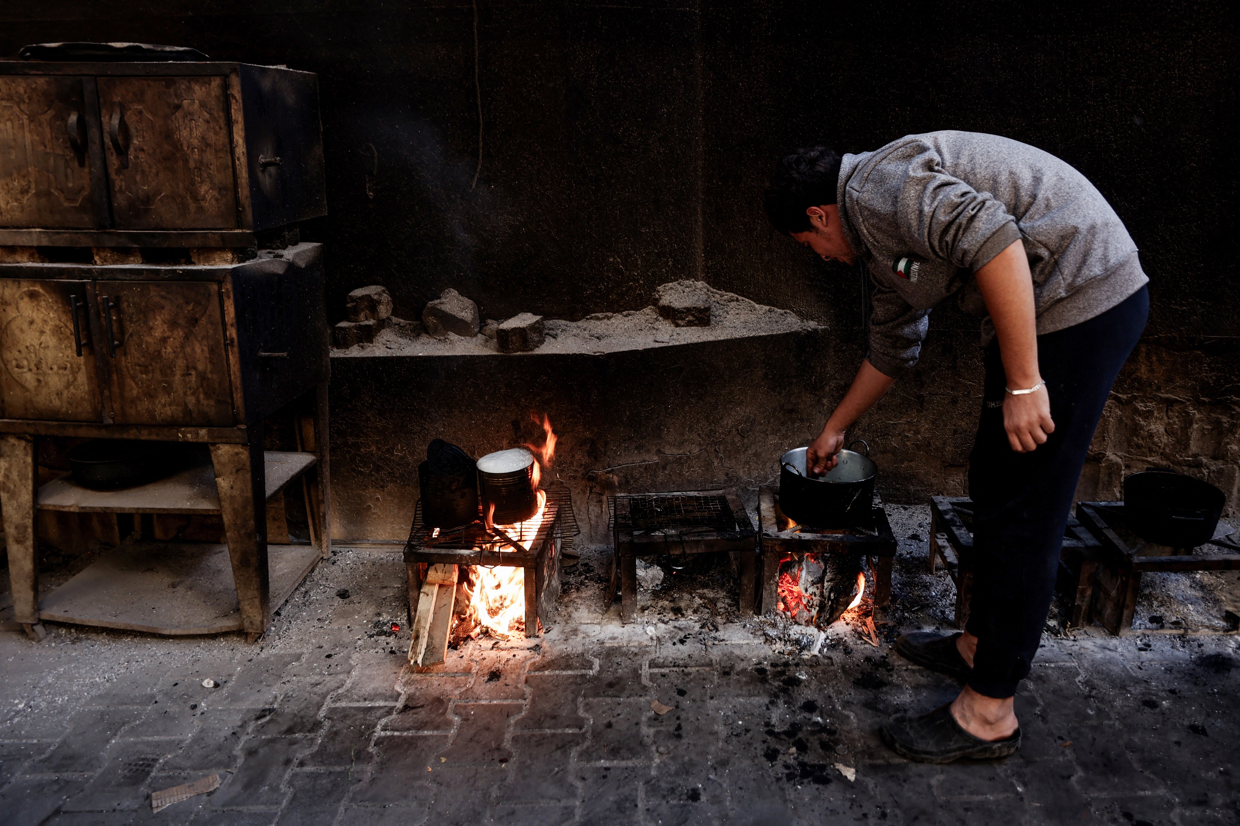 A displaced Palestinian man cooks food on a fire in a shelter inside the Holy Family Catholic Church compound