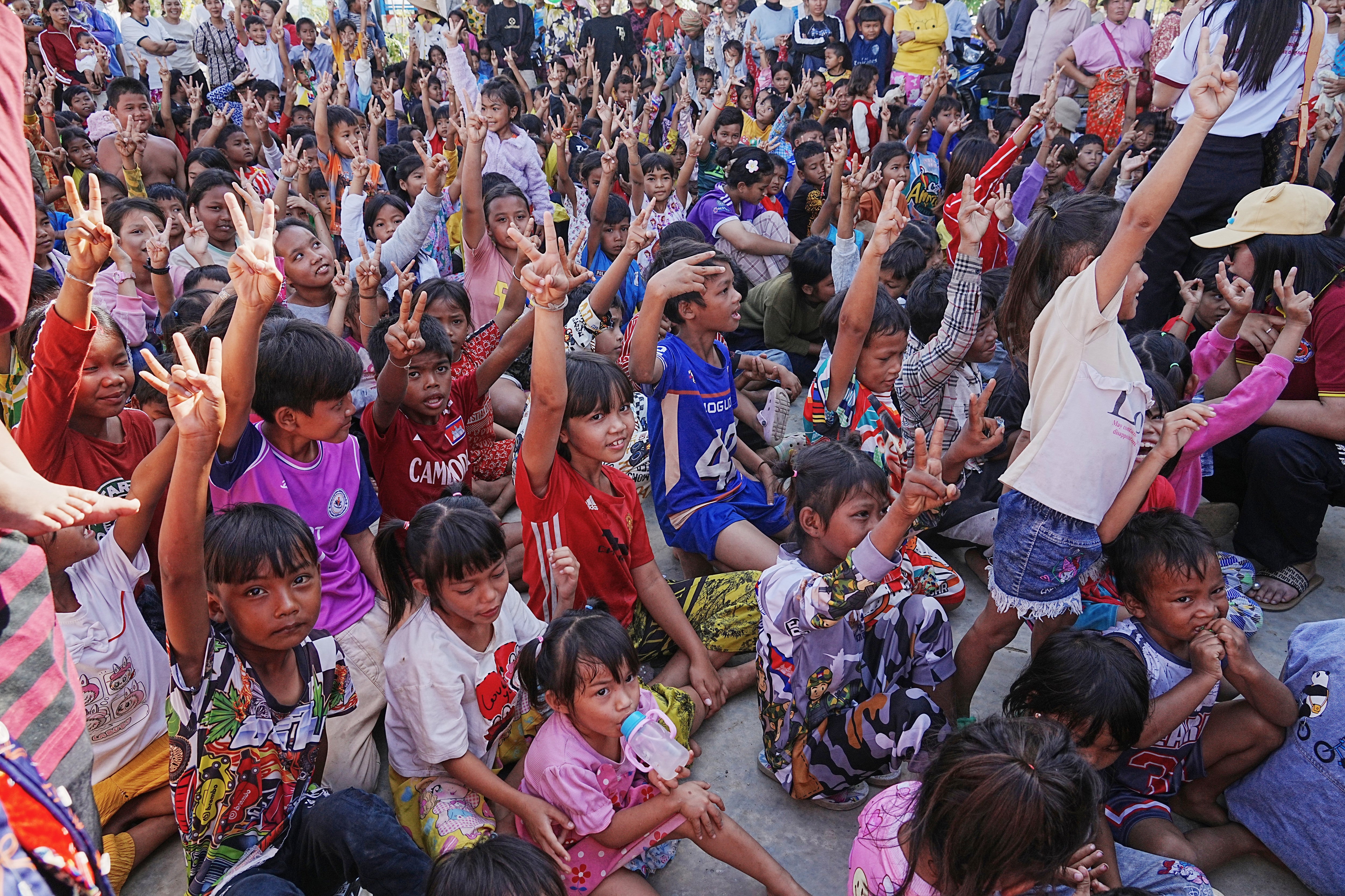 Children raise their hands while receiving donation from charity as they take refuge in Banteay Menchey provincial town, Cambodia, Saturday, 13 Dec 2025, after fleeing homes following fighting between Thailand and Cambodia
