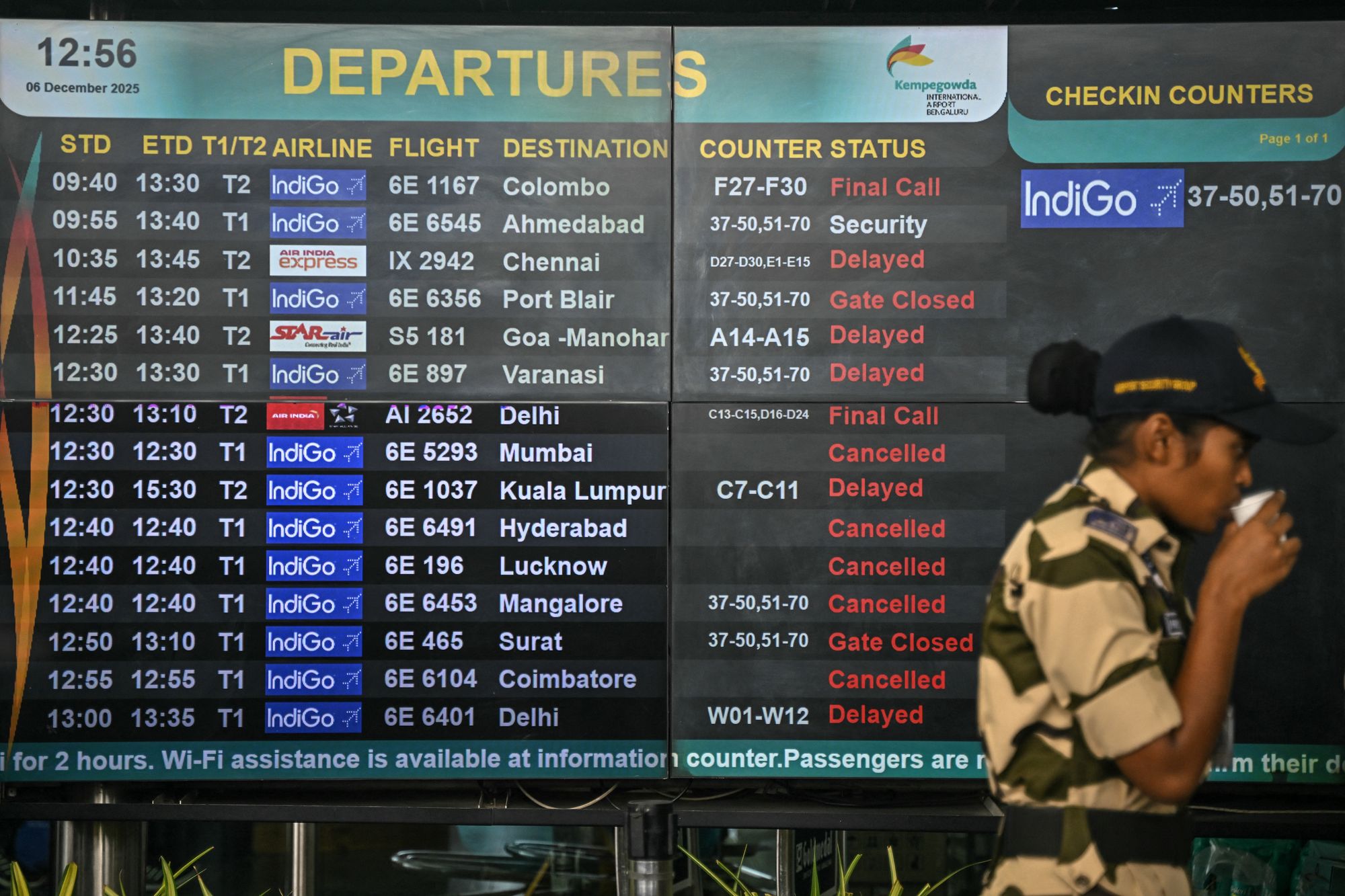 A security personnel stands beside a digital departures board at Kempegowda International Airport