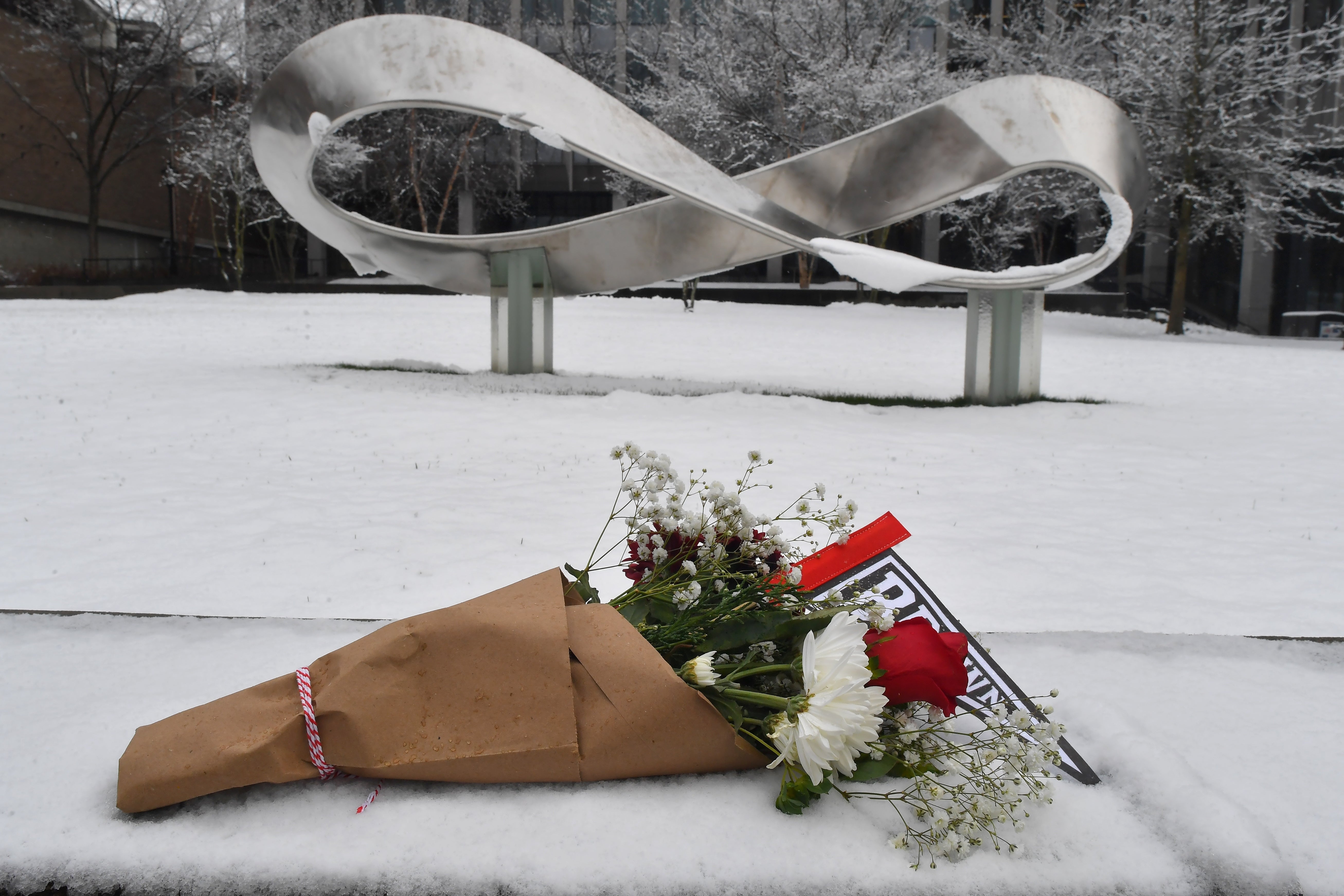 Flowers containing a Brown University pennant flag are laid in the snow less than a day after two students were killed in a mass shooting that injured nine others
