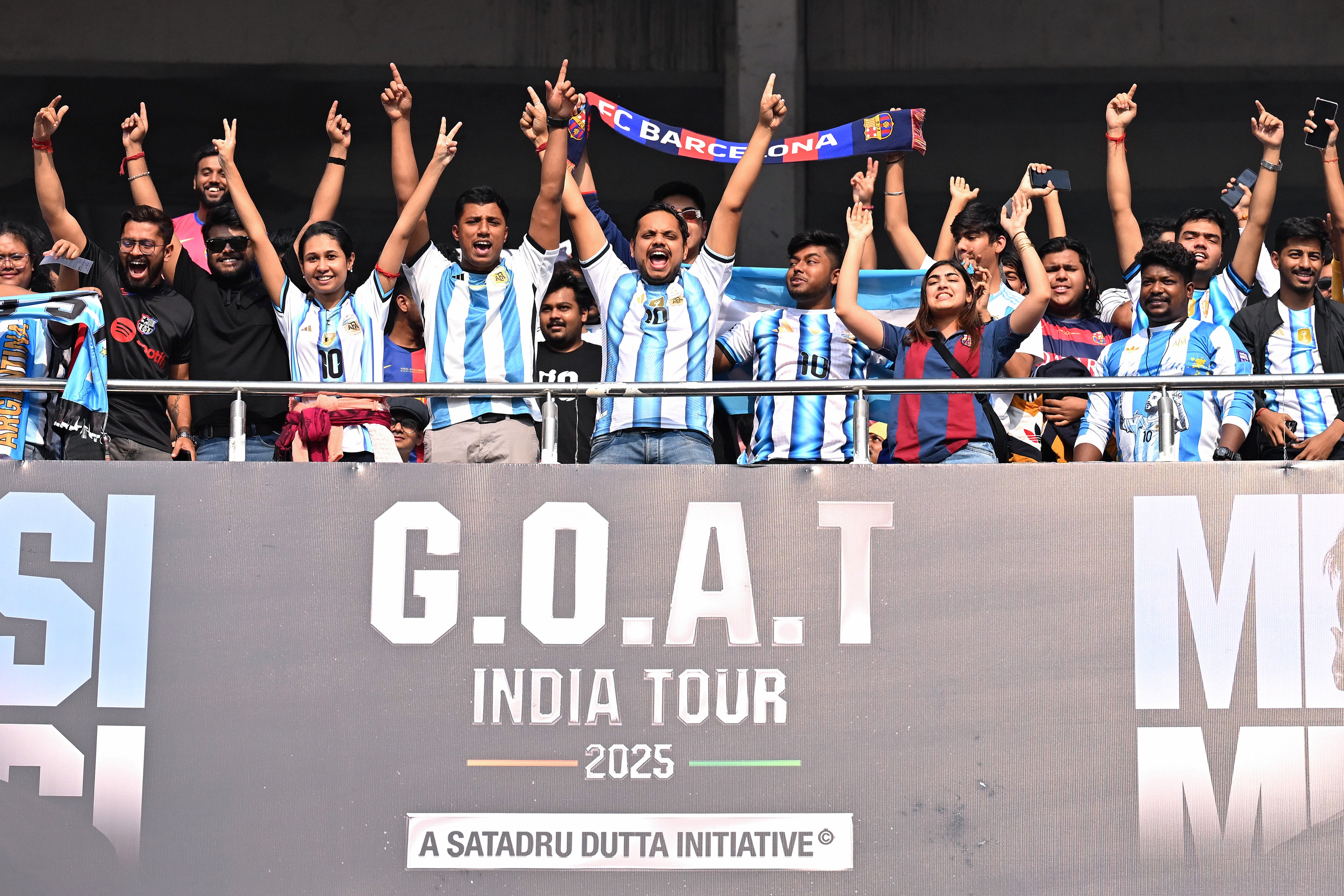 Fans of Lionel Messi cheer with flags and scarves at the stands in Kolkata
