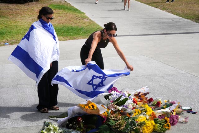 <p>A woman places an Israeli flag over flowers at Sydney’s Bondi Beach following the mass shooting that has claimed 15 lives</p>