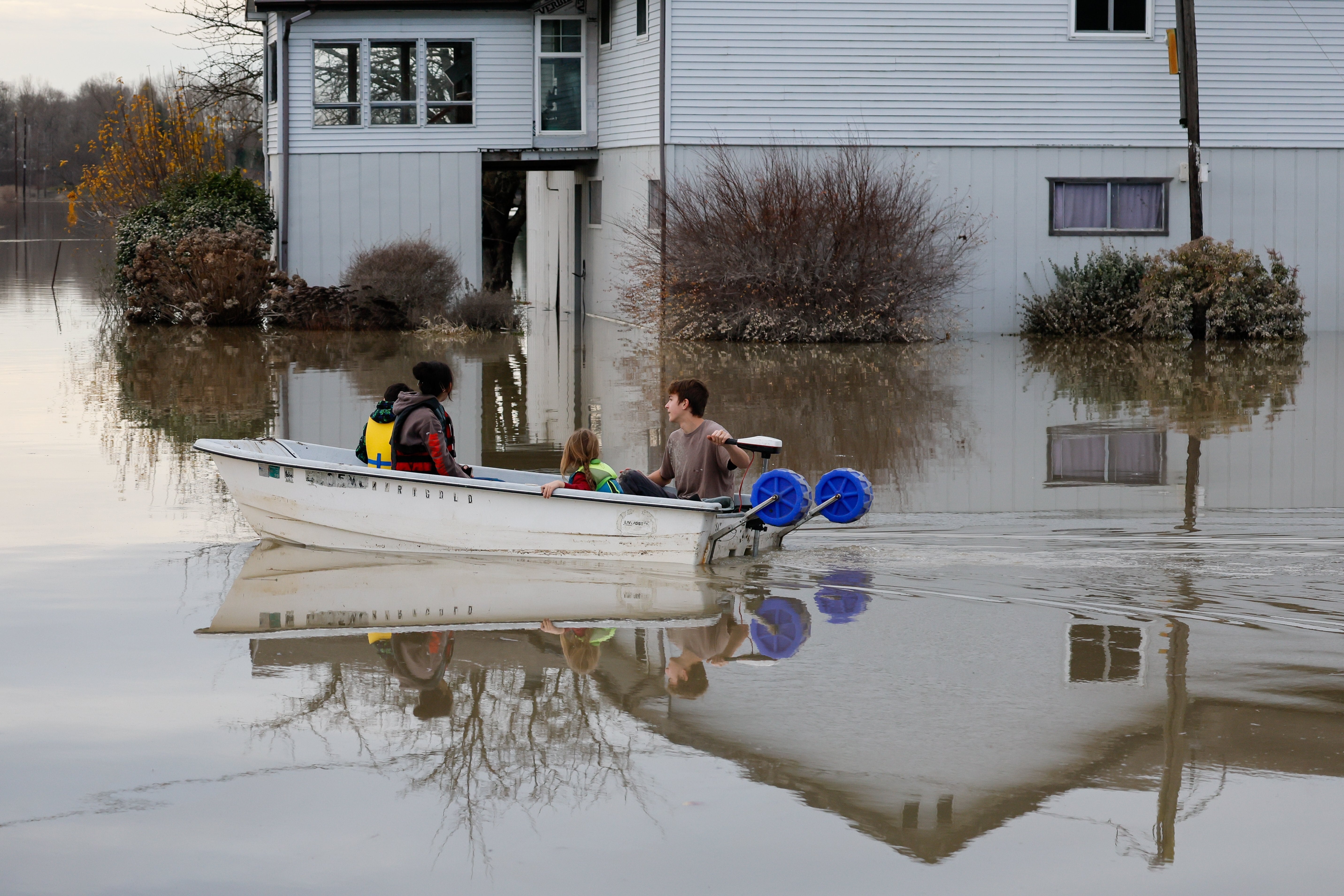 Carter Johnson, 16, uses a boat to transport his five-year-old brother, Milo, and two neighbors past a flooded house in what was their front yard Saturday, Dec. 13, 2025, near Clear Lake, Wash.