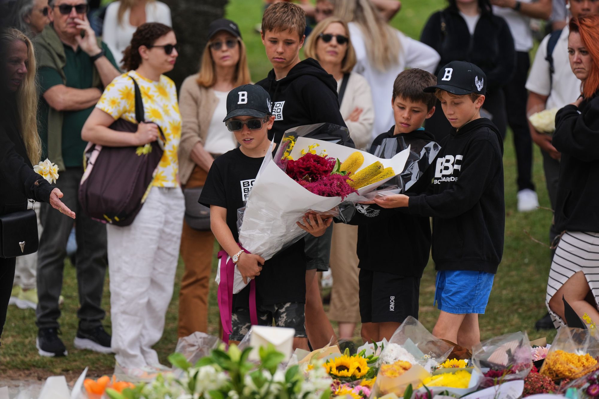Boys lay flowers at a flower memorial for victims of Sunday's shooting at the Bondi Pavilion at Bondi Beach on Tuesday, 16 December 2025, in Sydney, Australia