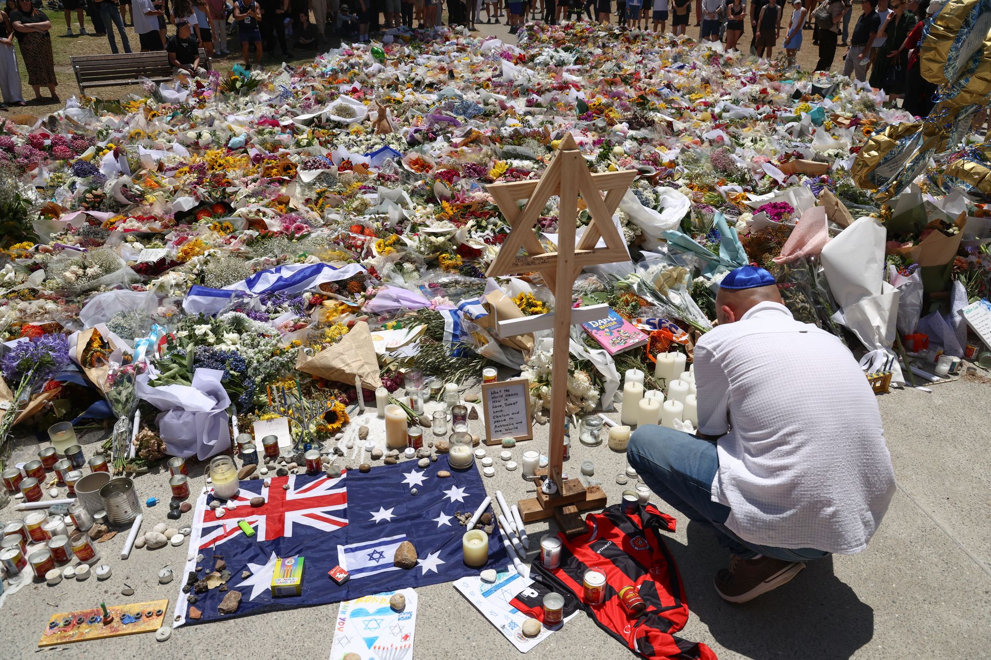 <p>A mourner lights candles as people gather around floral tributes outside Bondi Pavilion in Sydney on 17 December 2025, to honour victims of the Bondi Beach shooting</p>