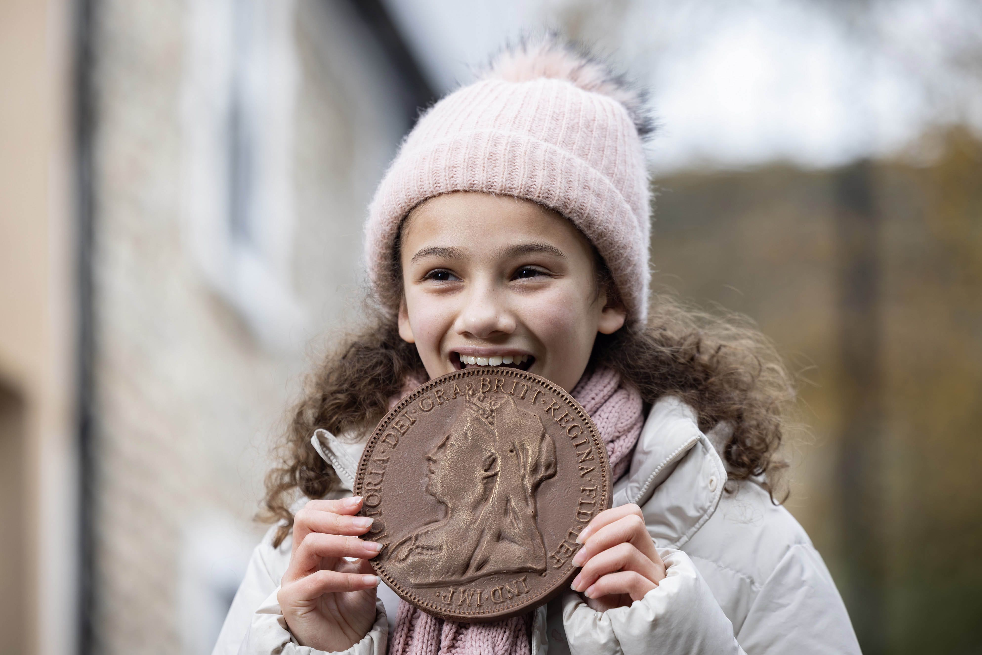 A girl takes a bite out of a chocolate coin as part of a collection of historical chocolate coins being unveiled to celebrate the opening of Cash Access UK’s 200th banking hub in Billericay, Essex (Matt Alexander/PA Media Assignments)