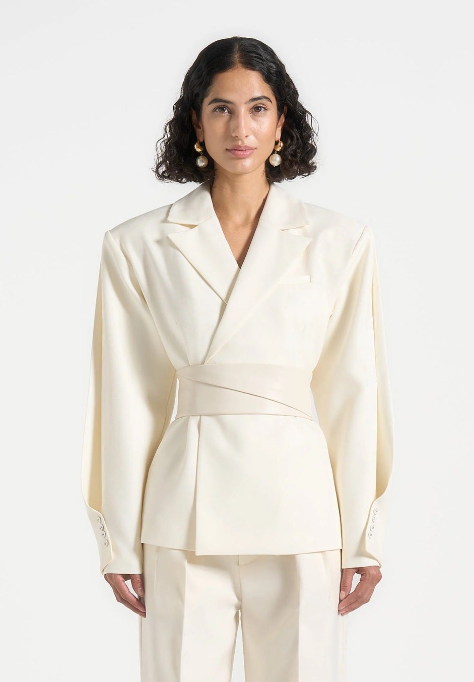 The model is wearing a cream-colored jacket with wide shoulders