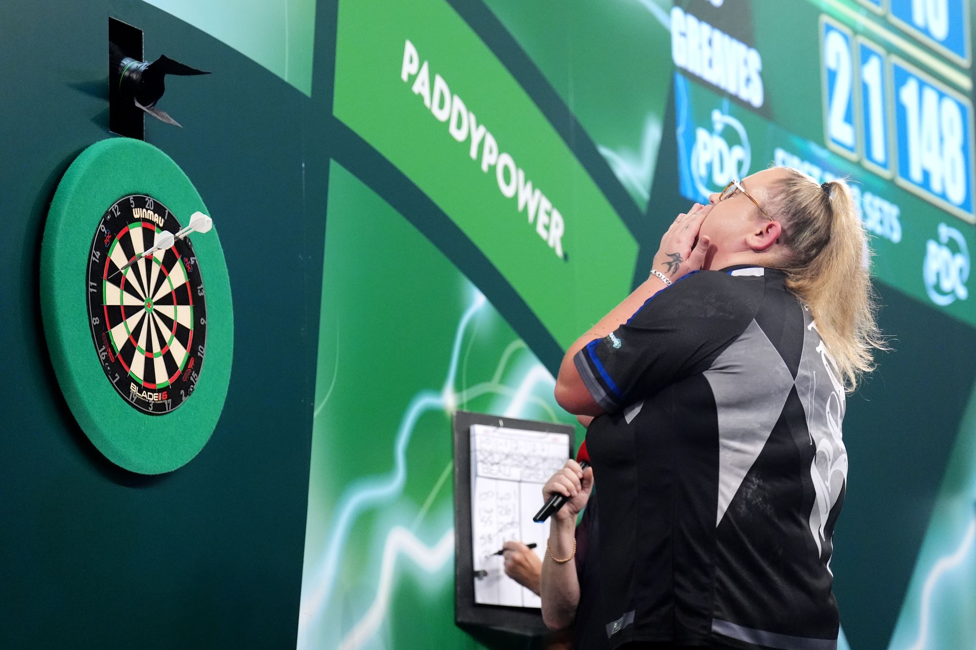 Beau Greaves on stage as a camera over the board captures her reaction